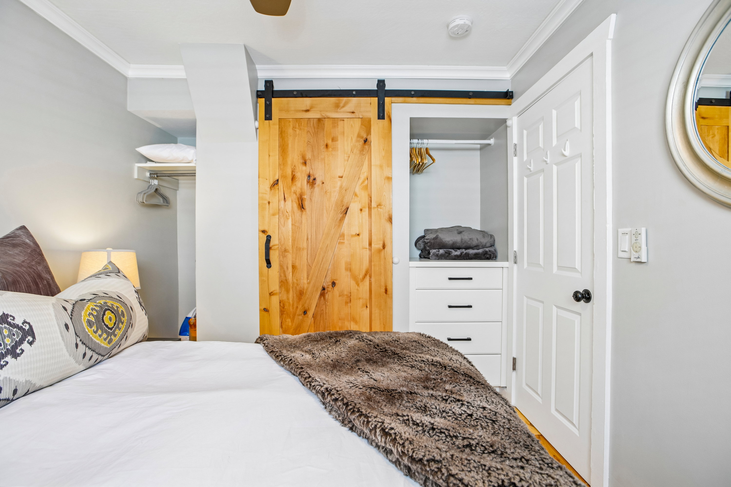 Built-in closet system featuring a natural wood barn door, white paneled door, and white drawer cabinetry with matte black hardware