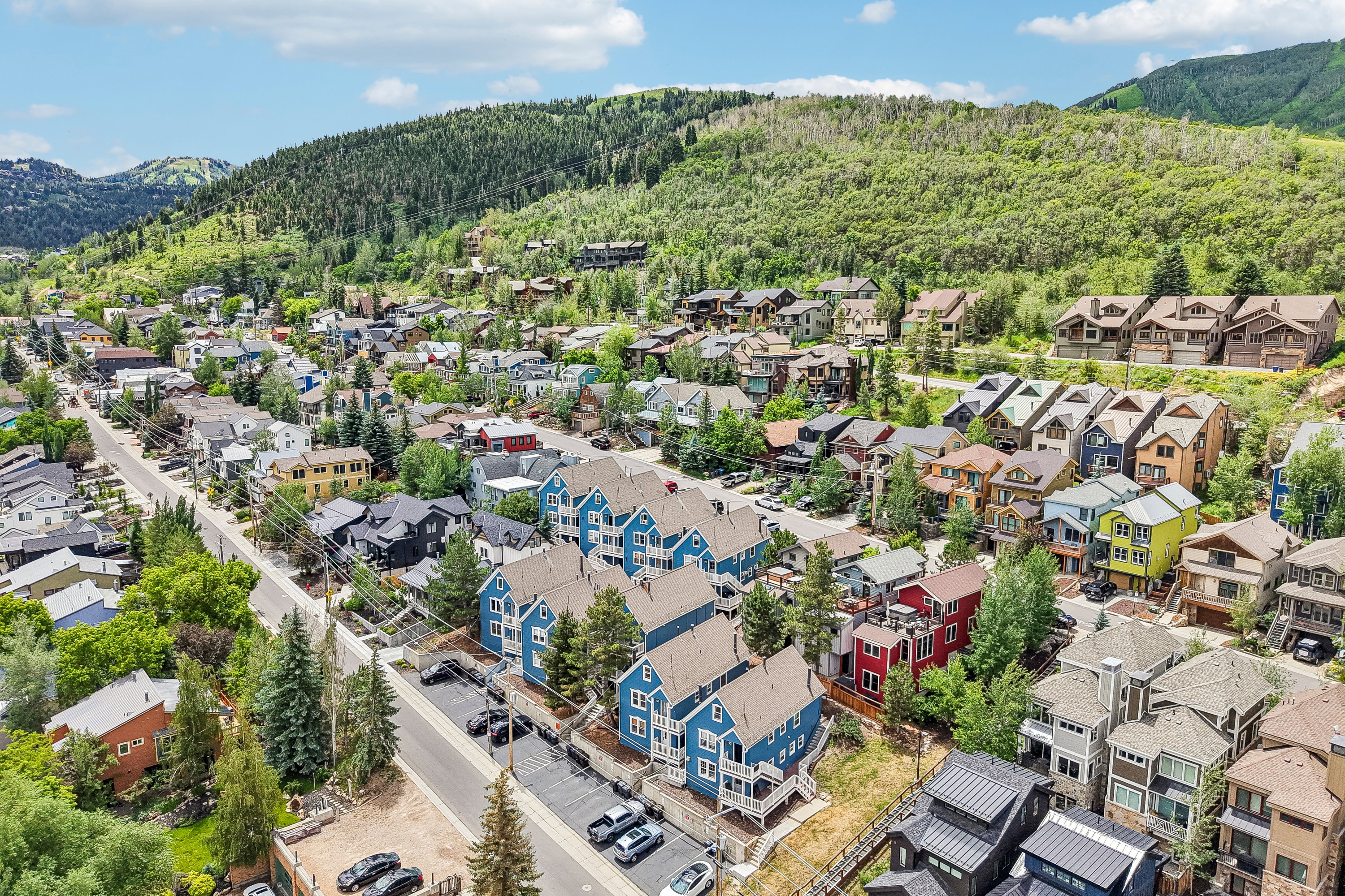 Expansive community setting featuring a collection of multi-story residences, varied architectural styles, lush green hillsides, mature trees, and a clear sky backdrop