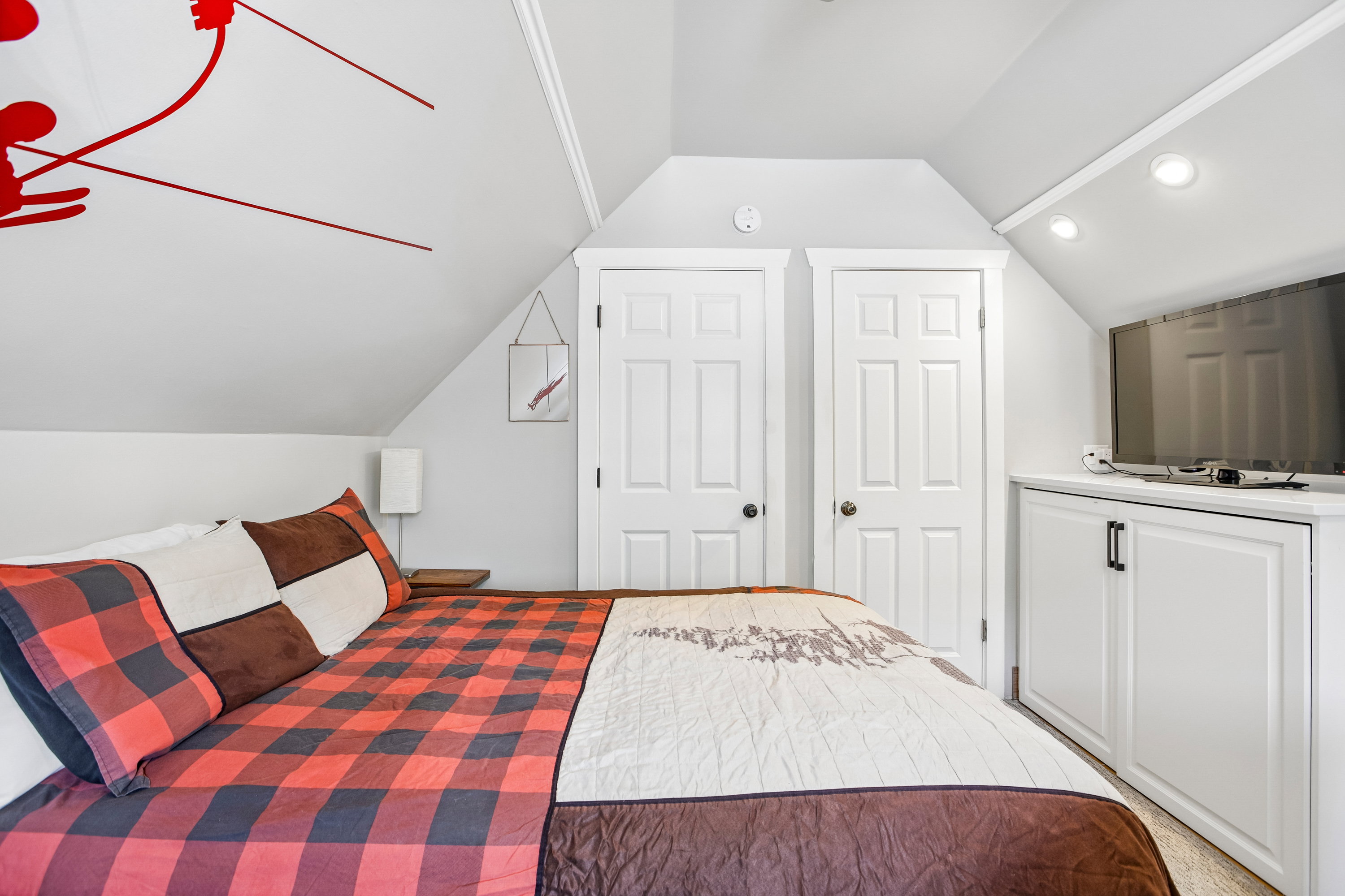 Sloped ceiling room featuring two paneled doors, built-in cabinetry with black hardware, and recessed lighting