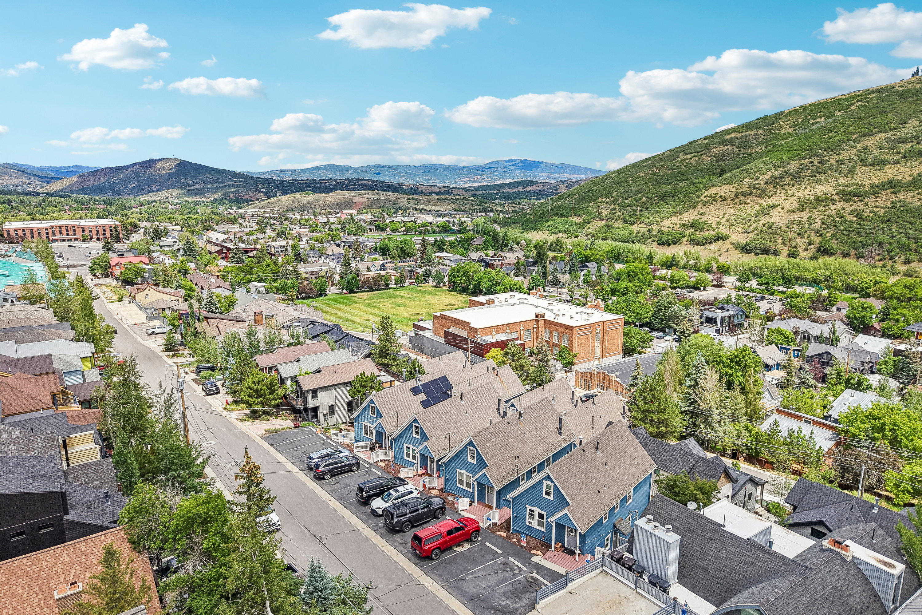 Aerial perspective showcasing a residential area with varied housing styles, surrounding green hills, and distant mountains