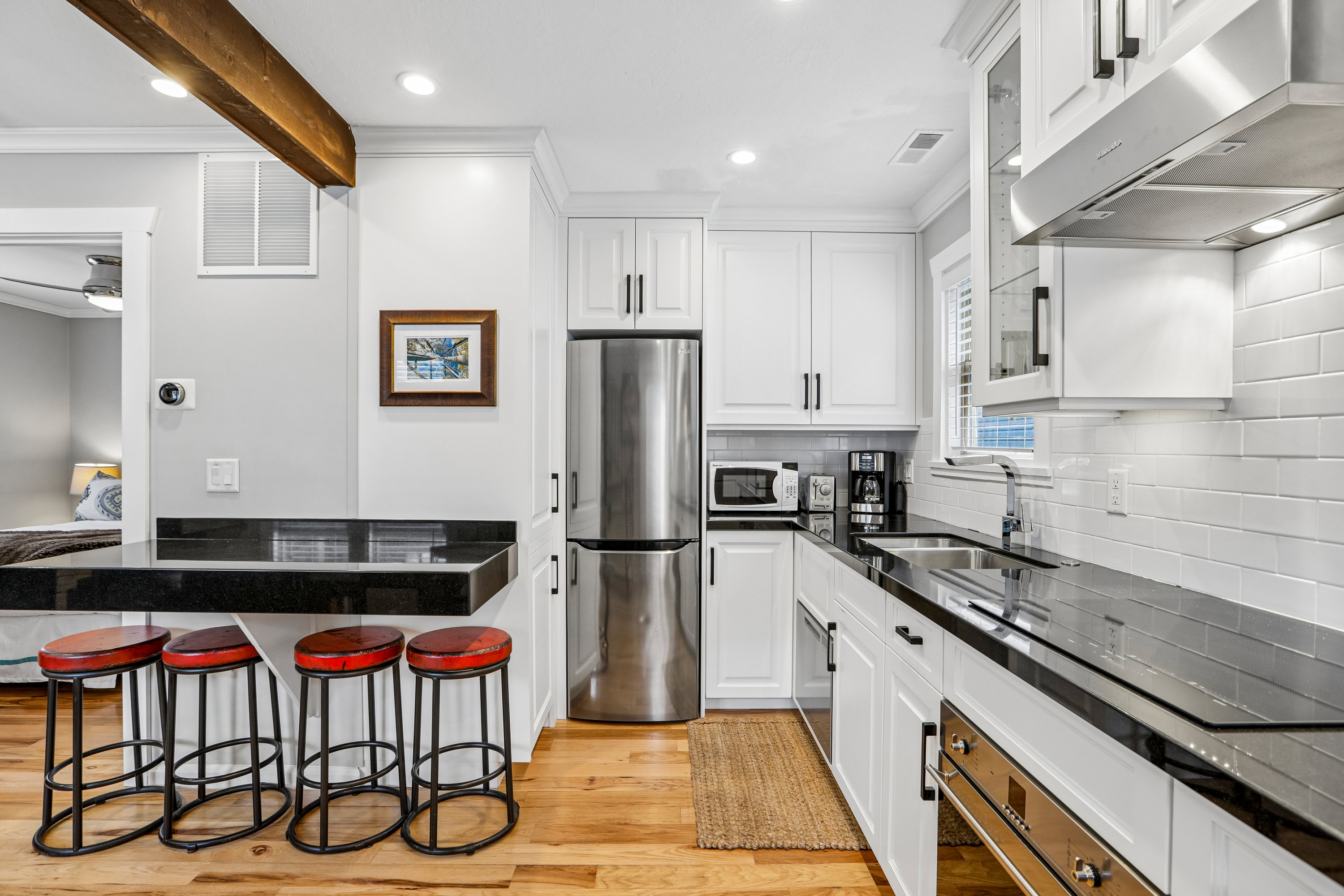 Contemporary kitchen featuring white shaker cabinetry, stainless steel appliances, dark countertops, a subway tile backsplash, and wood-finish flooring