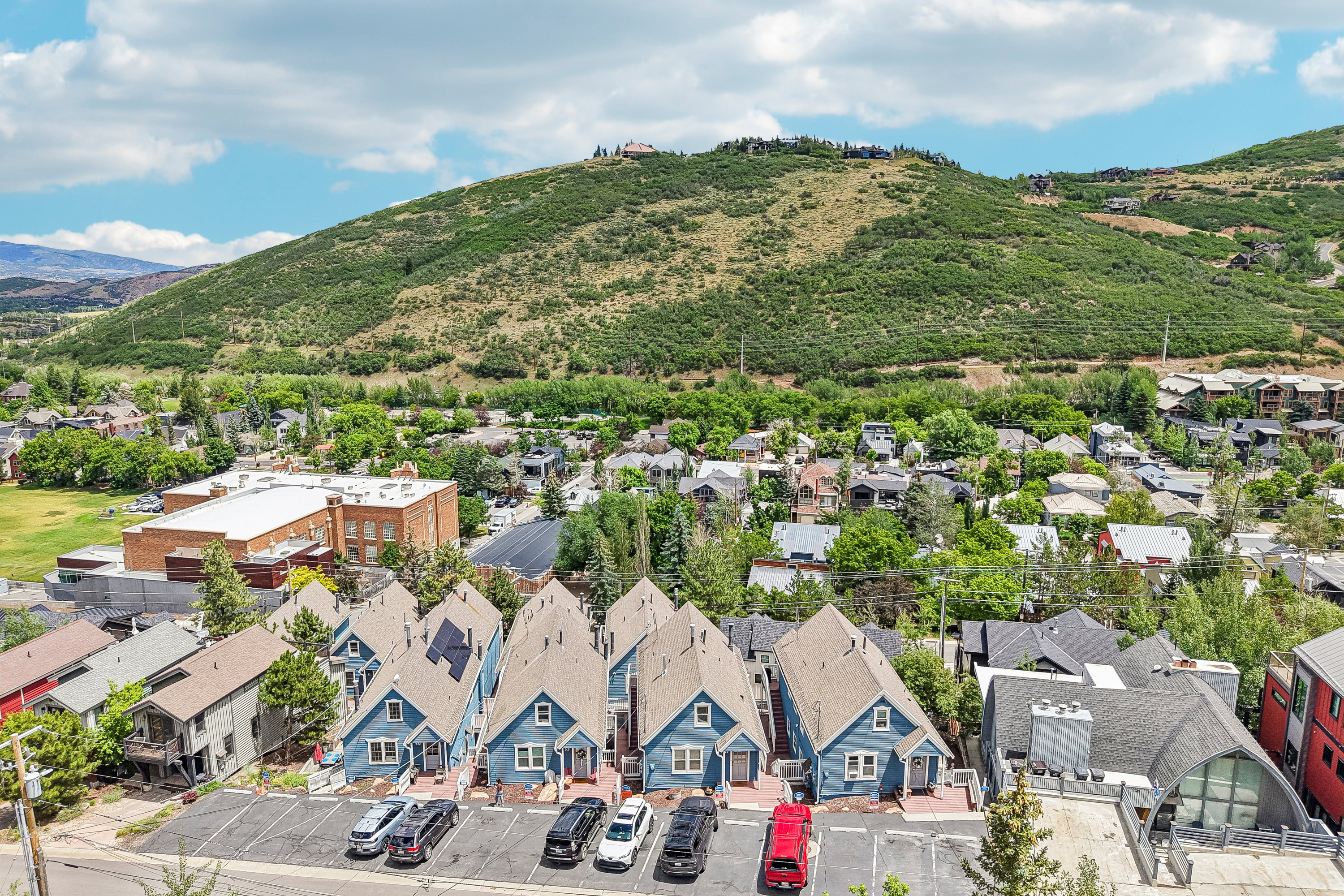 Row of blue residences with gabled roofs and individual parking spaces, set against a backdrop of verdant hills