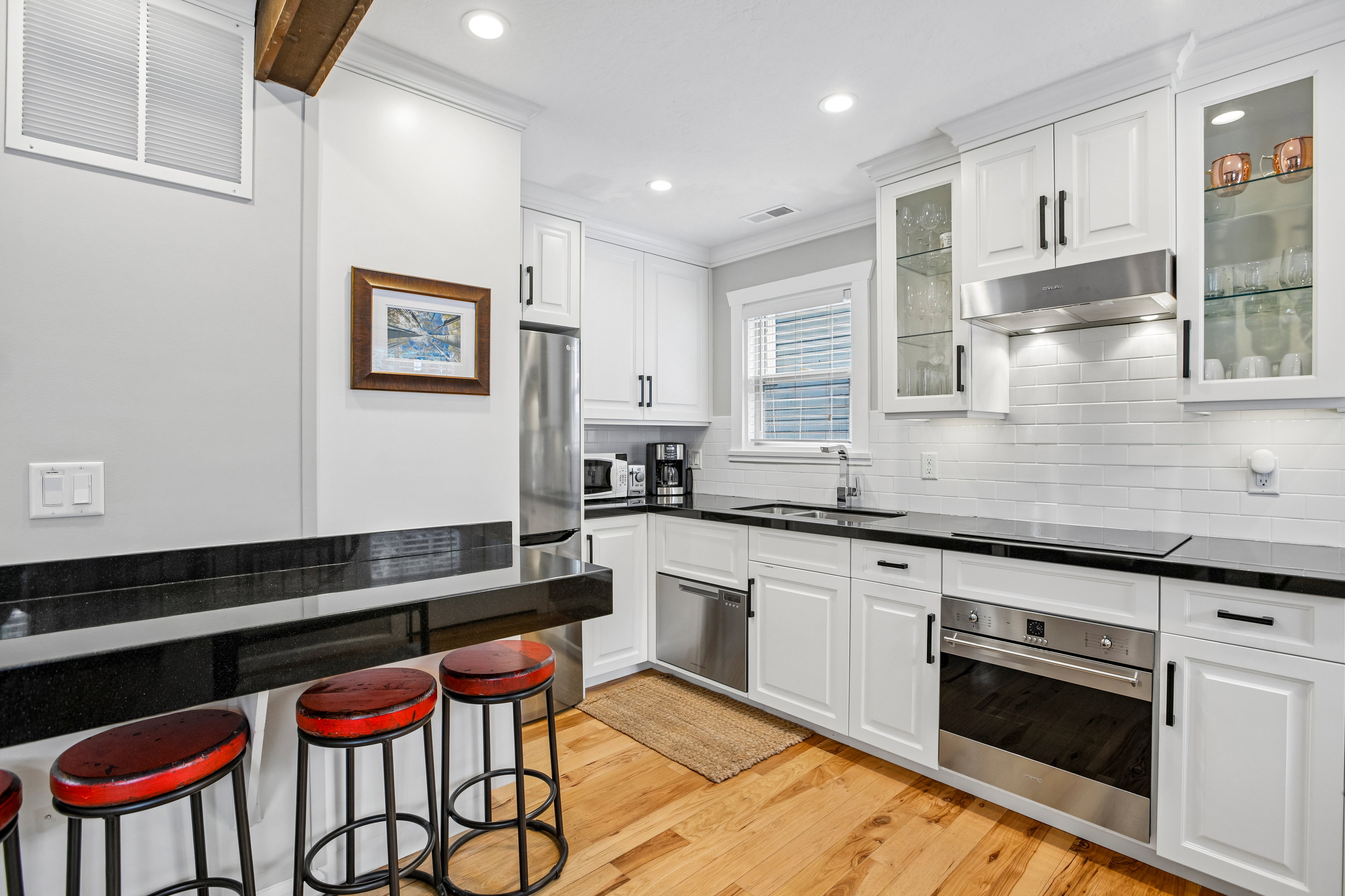 Modern kitchen featuring white cabinetry, stainless steel appliances, a subway tile backsplash, dark countertops, and wood-finish flooring