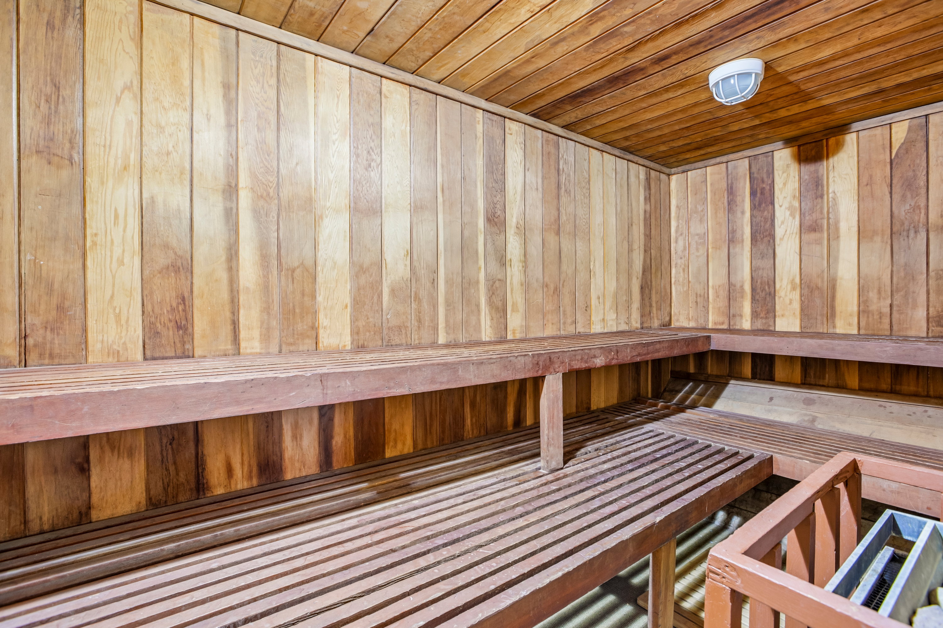 Custom sauna featuring natural wood paneling, slatted benches, and a flush-mount overhead light fixture