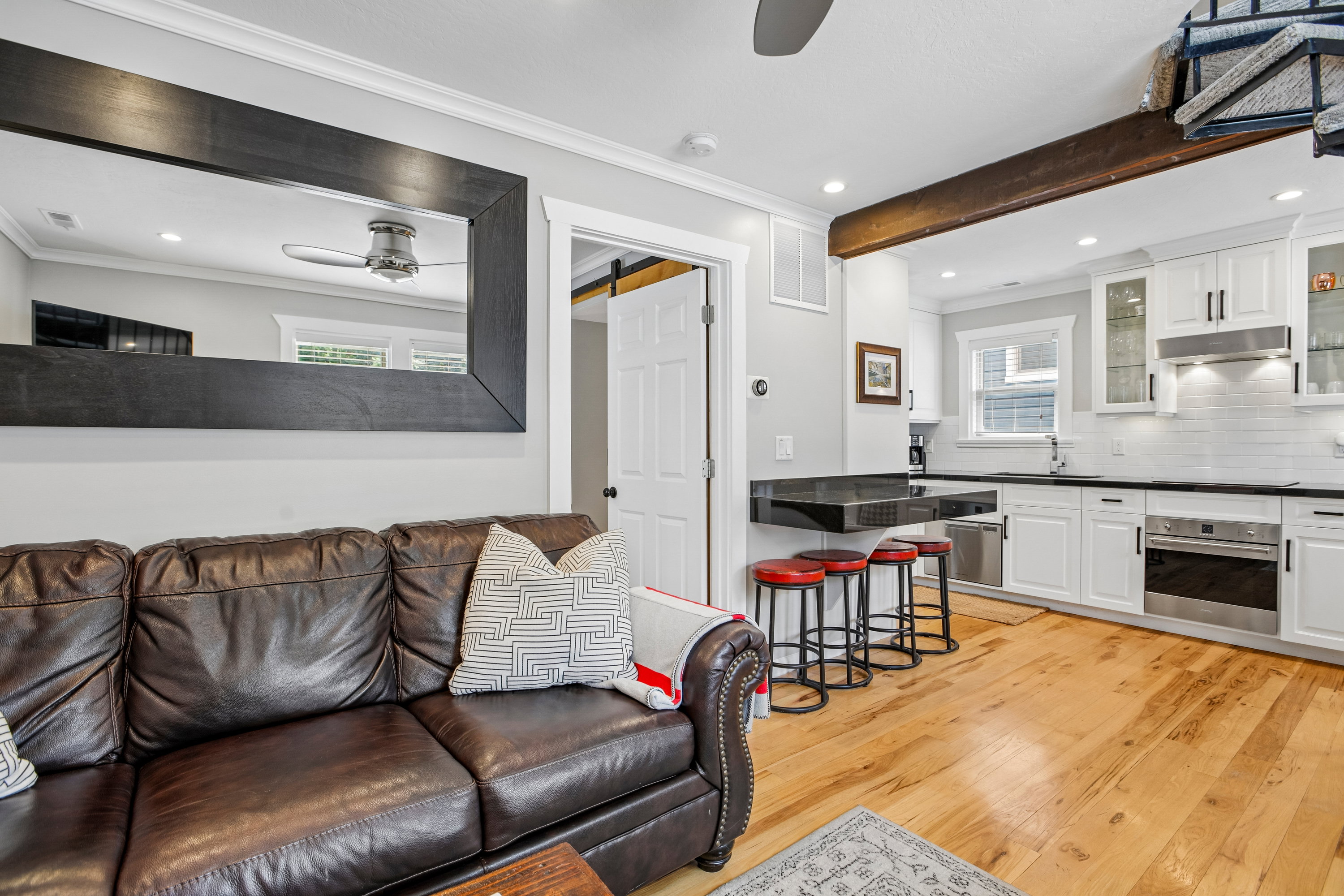 Open-concept living space featuring wood-finish flooring, a contemporary ceiling fan, and a kitchen with white cabinetry, stainless steel appliances, and a black countertop with breakfast bar seating