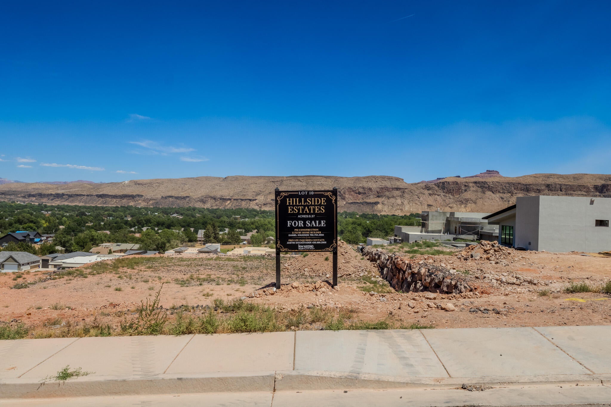 Expansive developable lot featuring a prominent "For Sale" sign, a concrete curb, and a distinct rock retaining wall