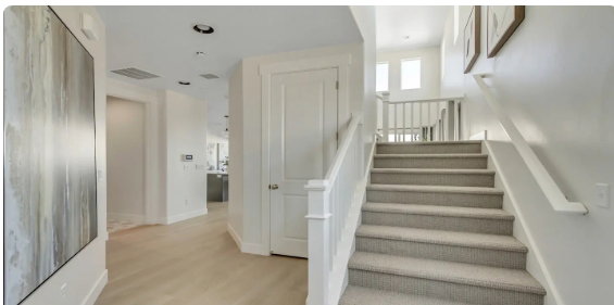 Carpeted staircase with white railings, featuring recessed lighting, light wood-finish flooring, a white paneled door, and a thermostat. PICTURE IS OF A SIMILAR HOME