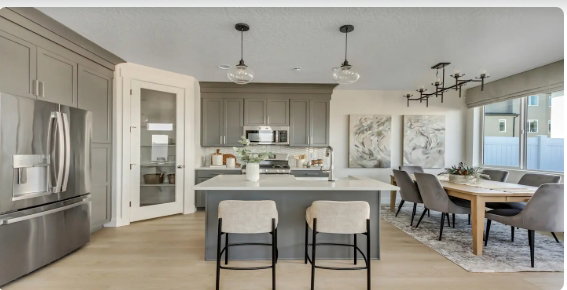 Open-concept kitchen and dining area featuring light wood-finish flooring, gray shaker cabinetry, and a central island with a light-colored countertop. PICTURE IS OF A SIMILAR HOME
