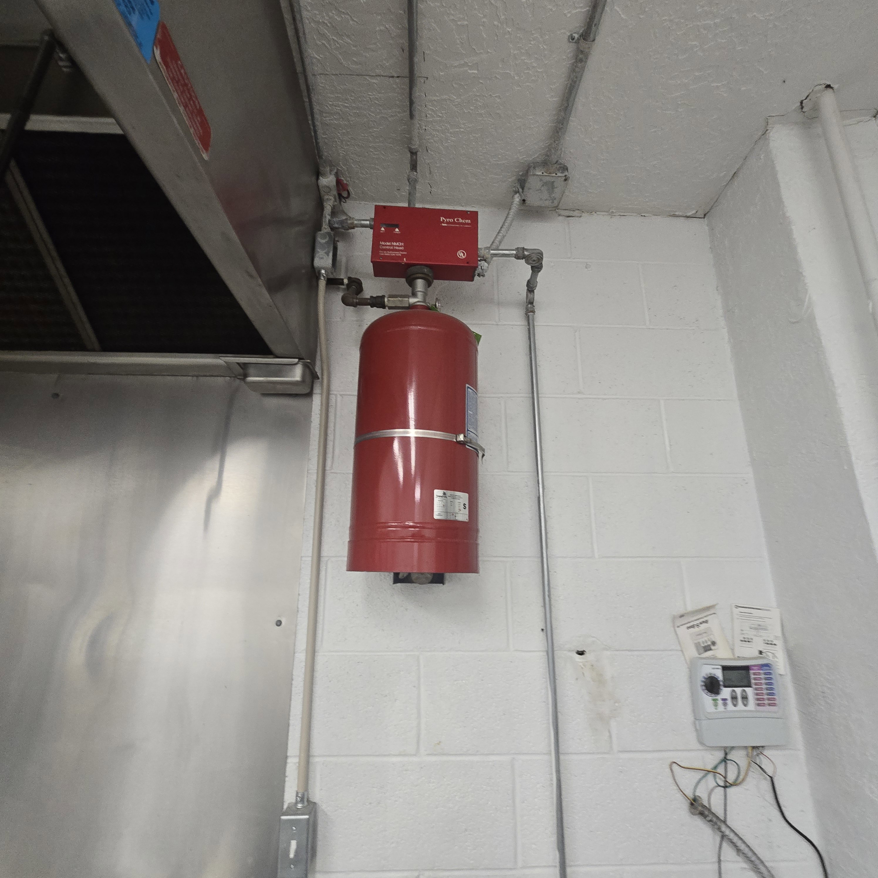 Commercial-grade stainless steel exhaust hood and a wall-mounted fire suppression system with a red cylinder and control panel