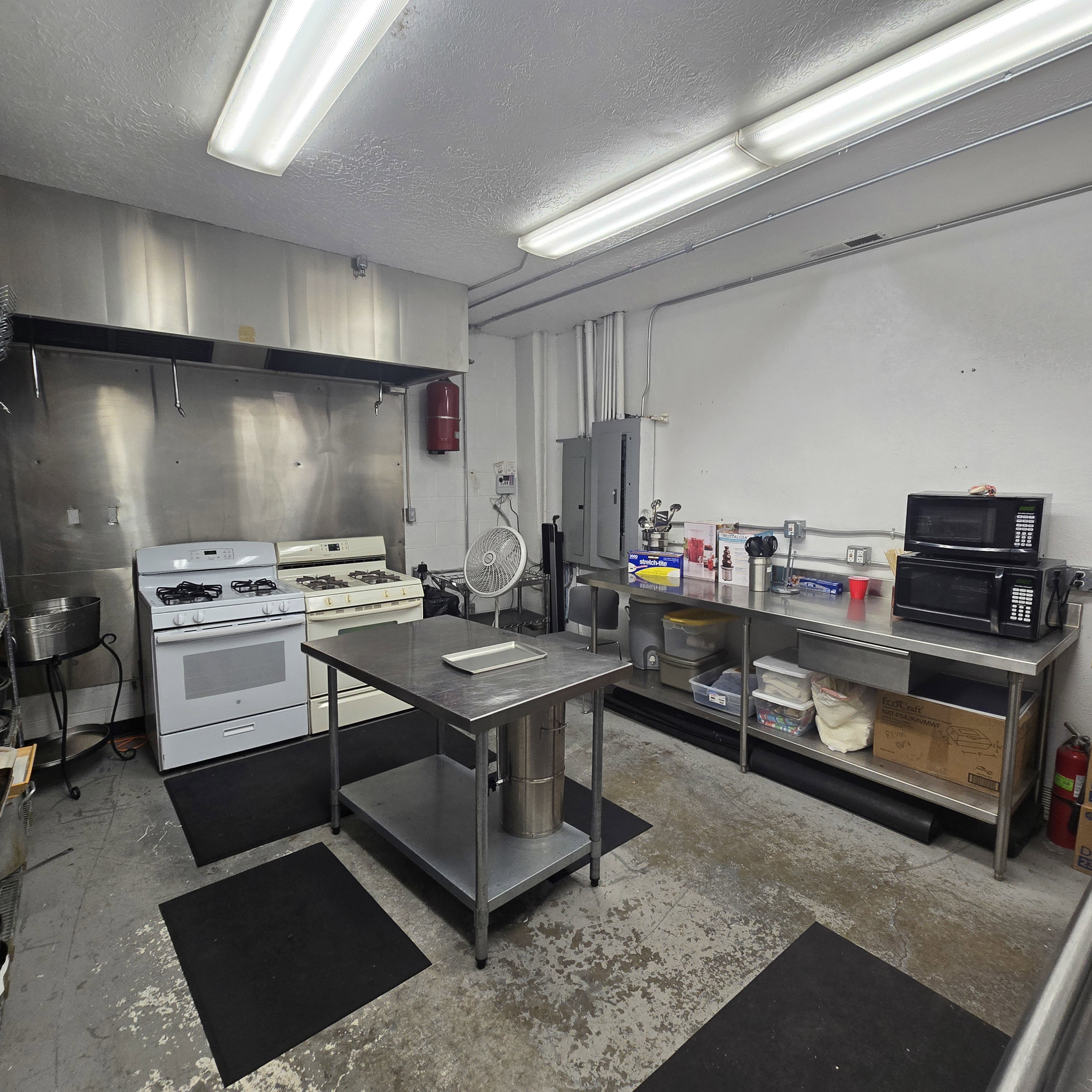 Commercial kitchen space featuring two gas ranges with a stainless steel vent hood, extensive stainless steel countertops, and a central stainless steel prep table