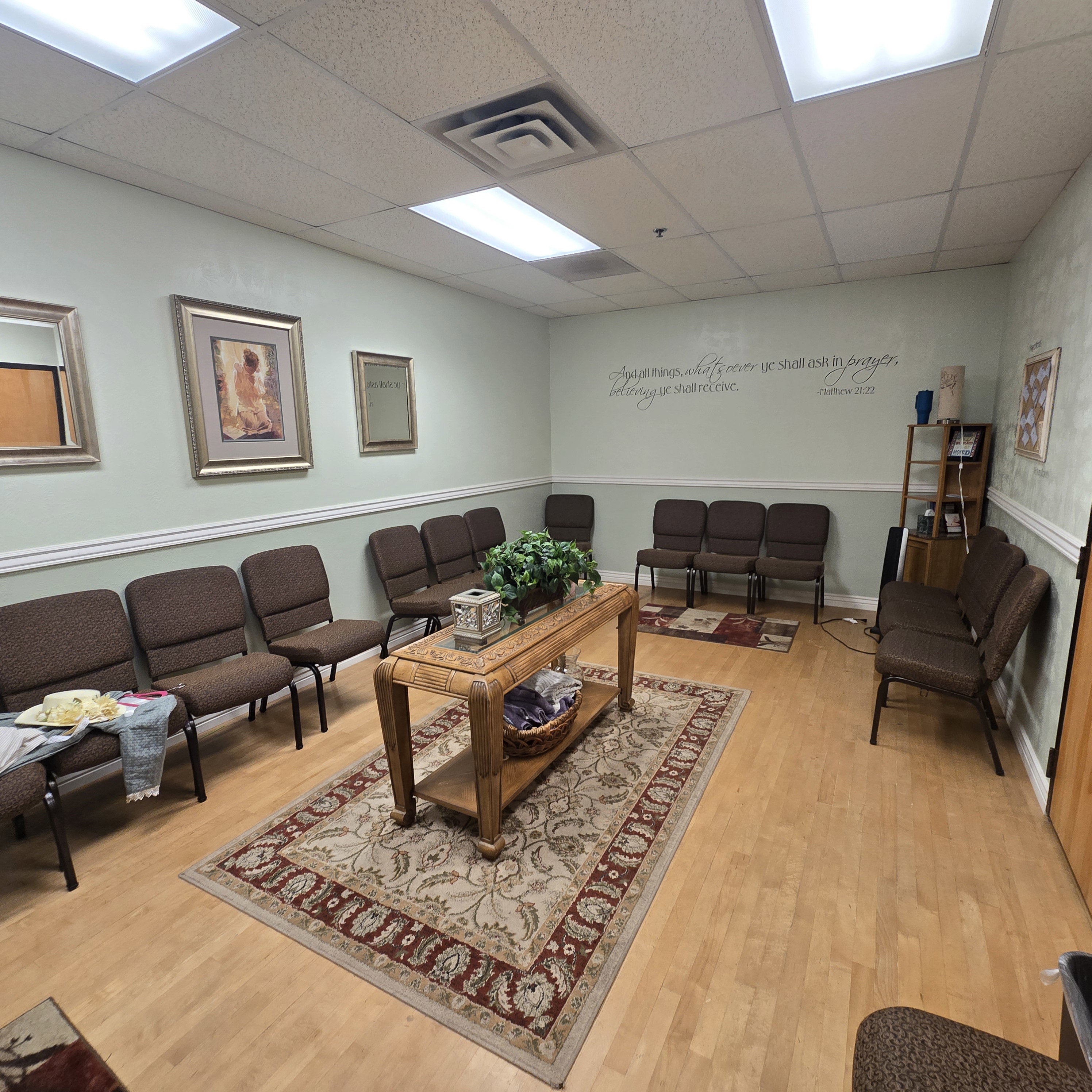 Spacious waiting area featuring light wood-finish flooring, a drop ceiling with recessed lighting, and pale green walls with white chair rail molding