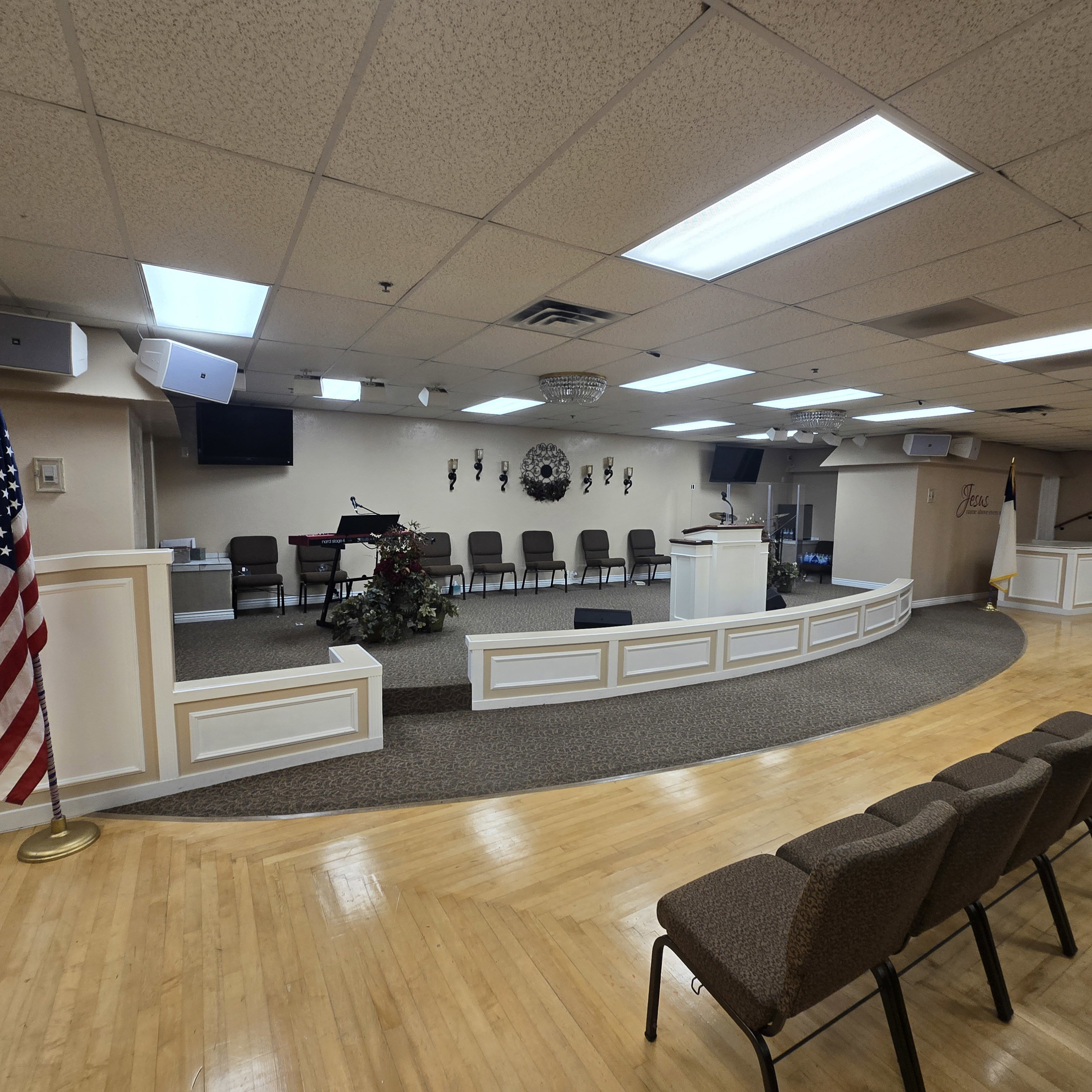 Spacious assembly room featuring a raised platform with white paneling and a carpeted stage area