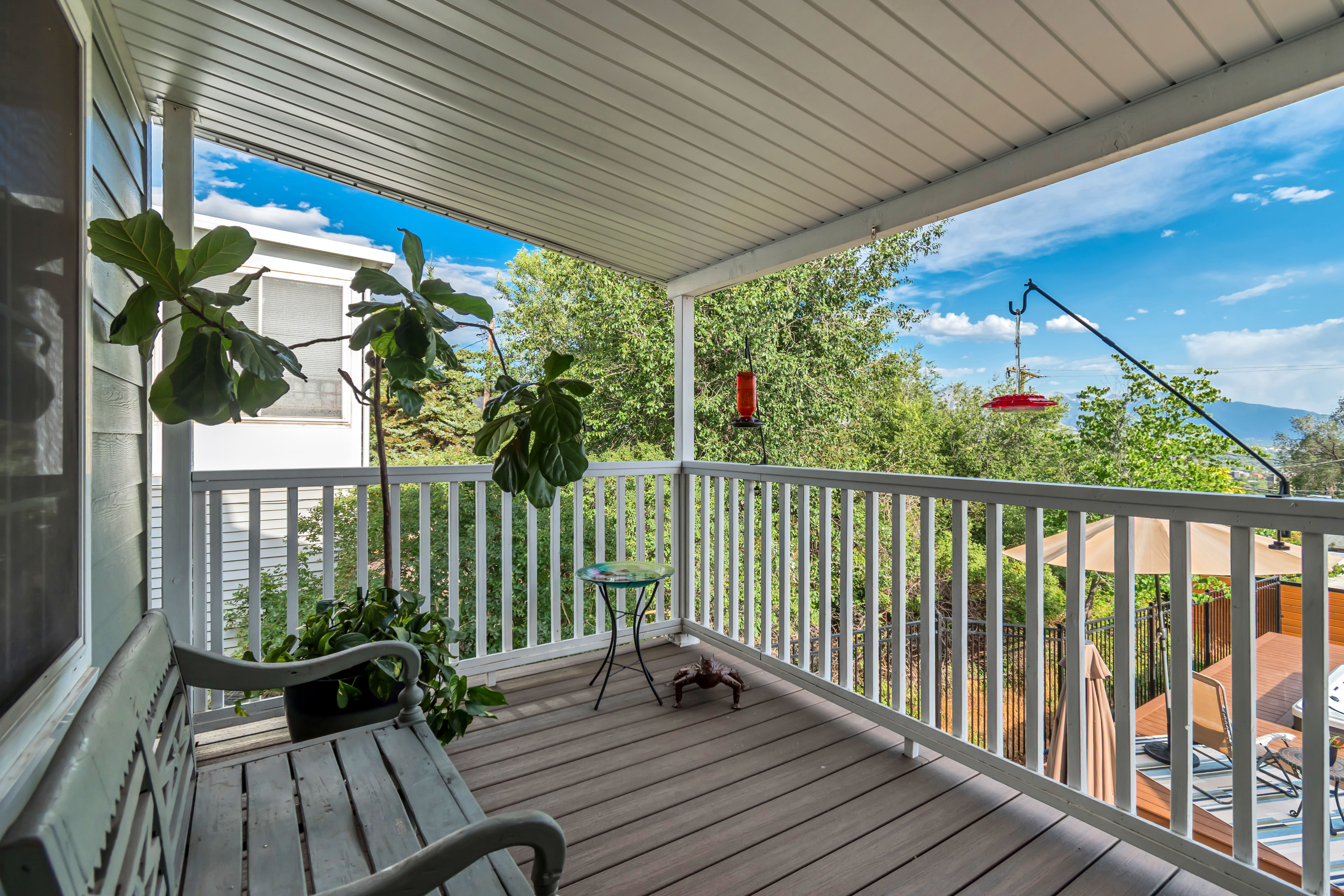 Covered outdoor deck with composite decking and white railing overlooking mature trees