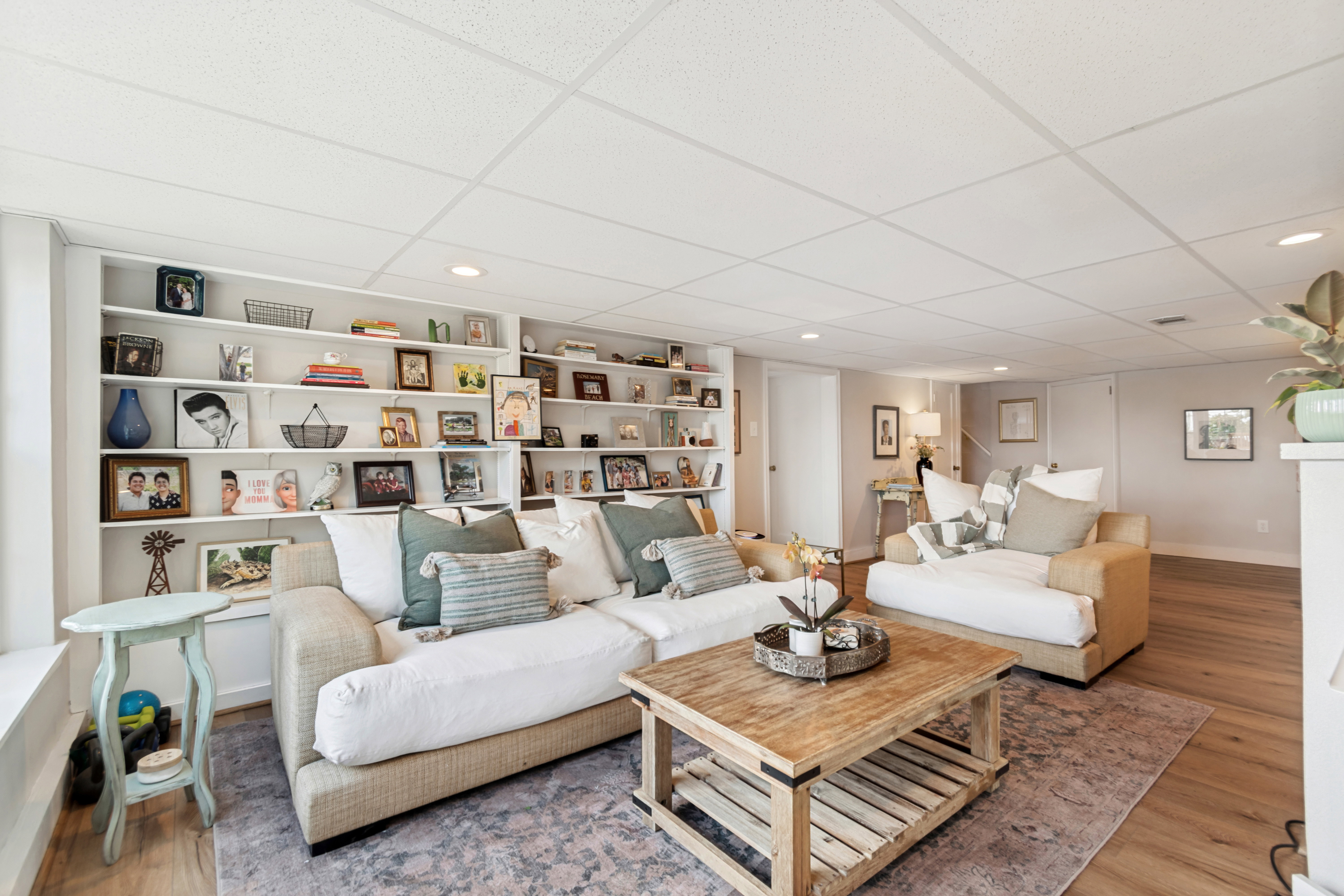 Spacious living area featuring extensive built-in shelving, recessed lighting, wood-finish flooring, and a drop ceiling