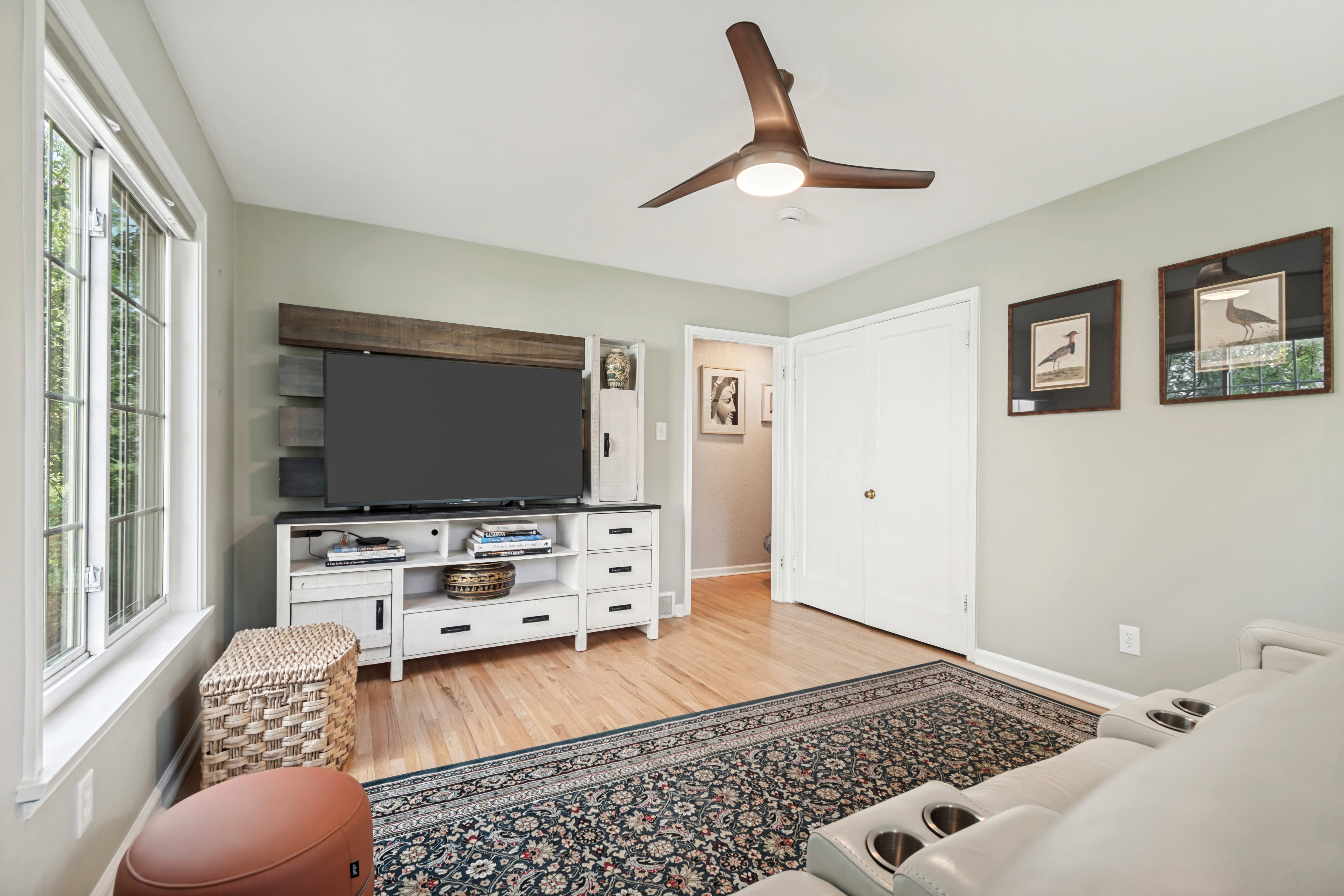 Hardwood flooring in a room featuring a modern ceiling fan with integrated lighting, a grid-pattern window, and white bi-fold closet doors