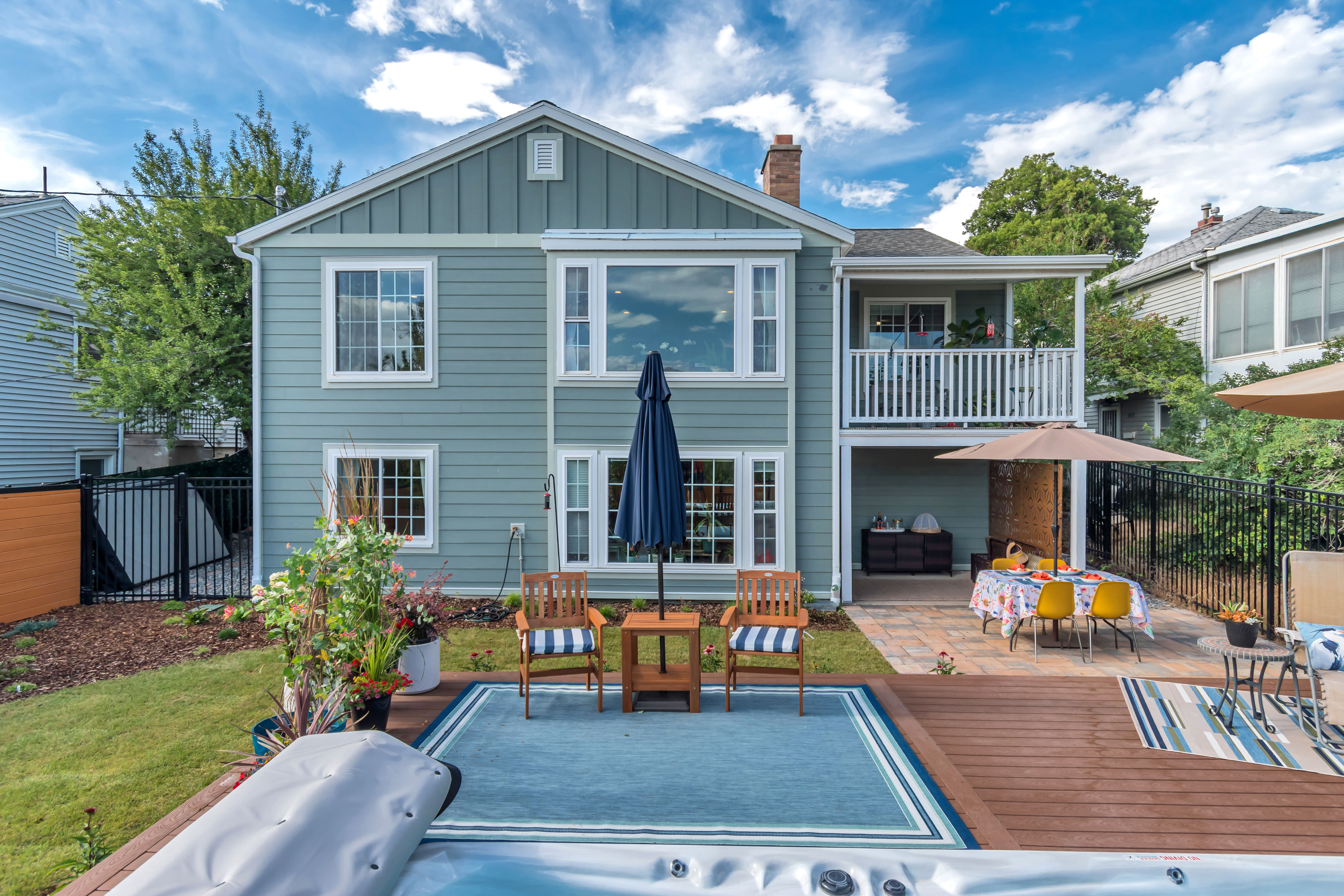 Rear exterior featuring light blue siding, a second-story balcony with white railings, and a ground-level patio