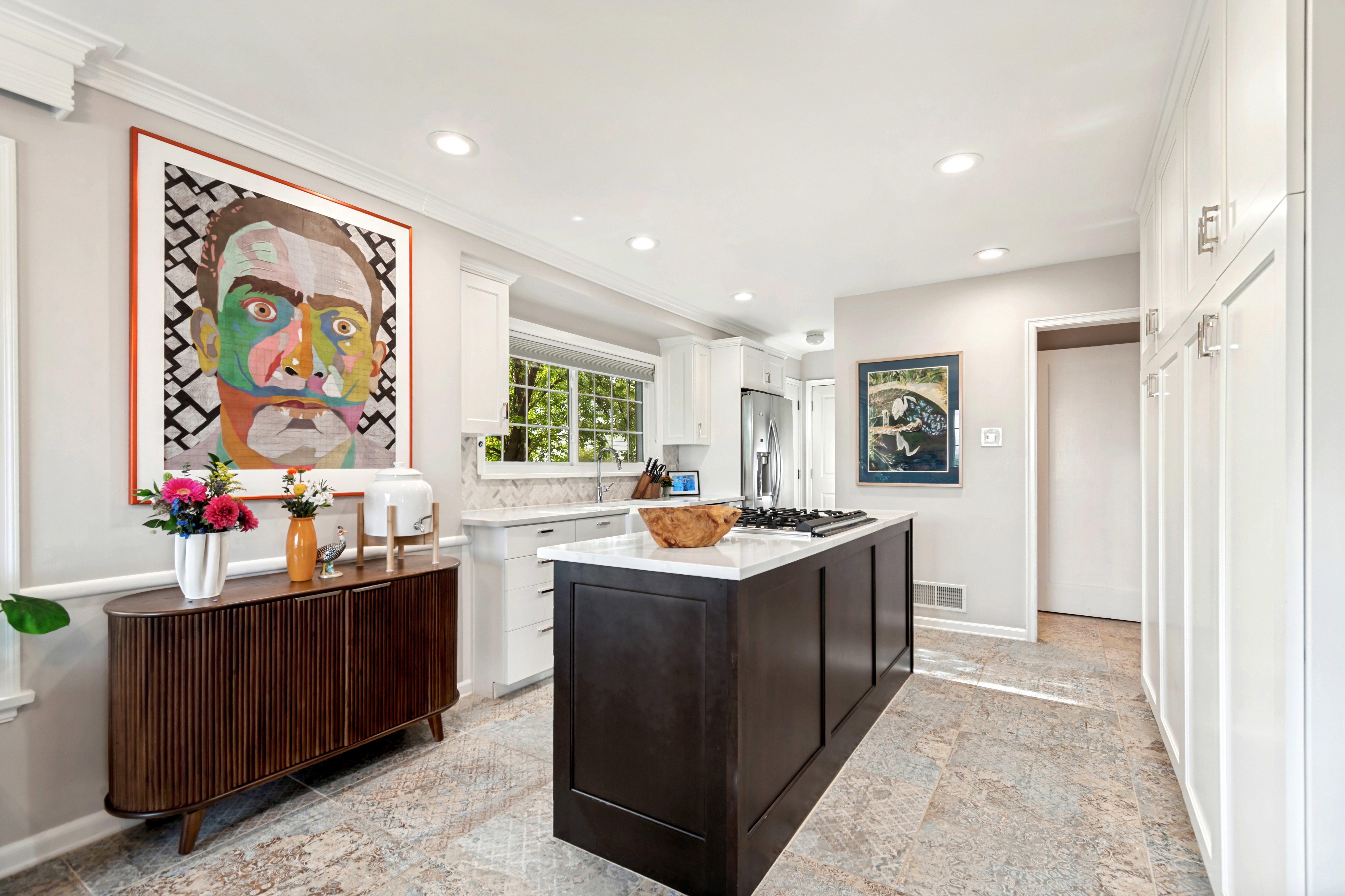 Spacious kitchen featuring an expansive center island with a cooktop, white perimeter cabinetry, light-toned flooring, recessed lighting, and a window above the sink