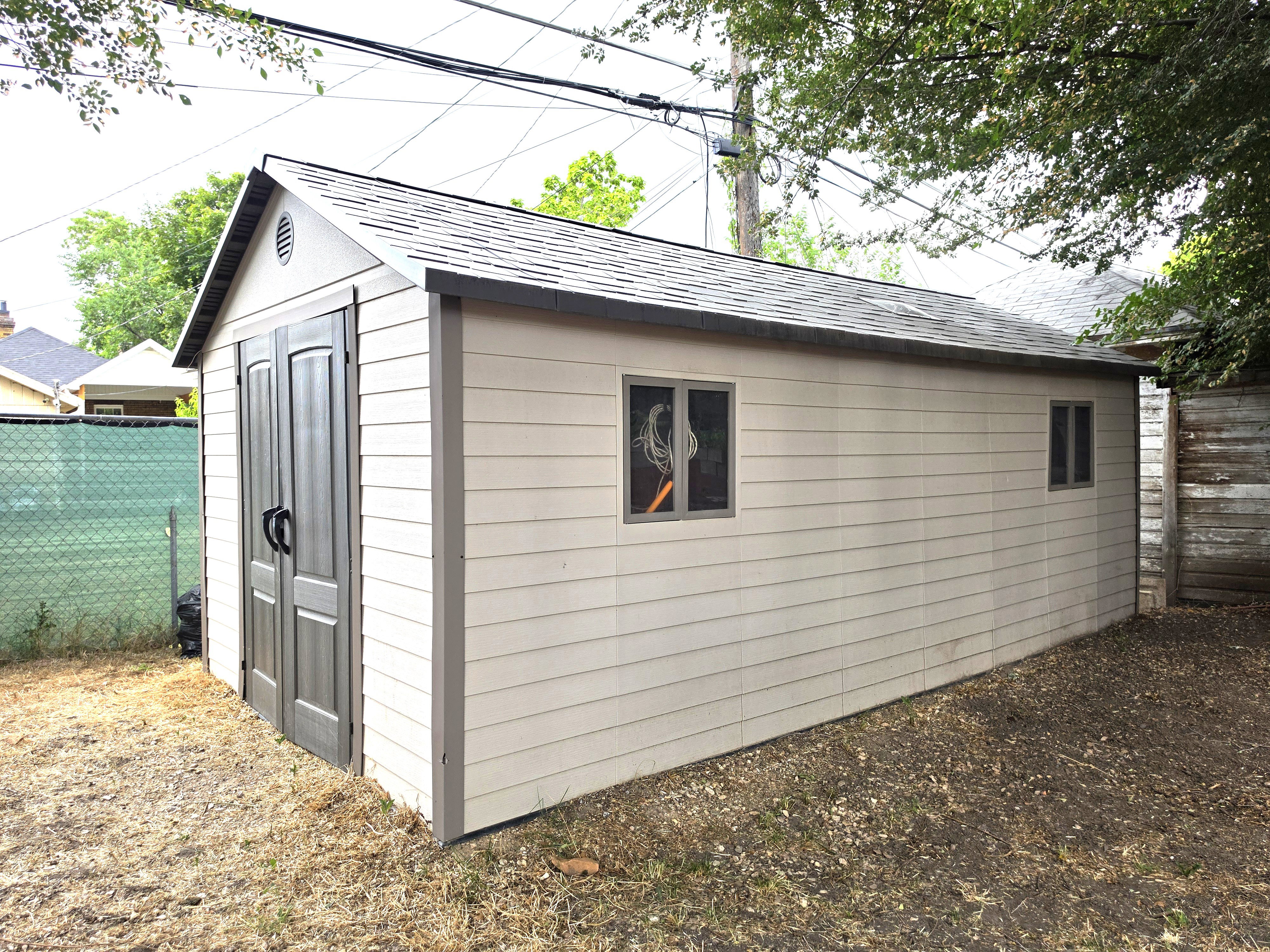 Detached storage shed with dual front entry doors, shingle roof, two windows, and horizontal siding