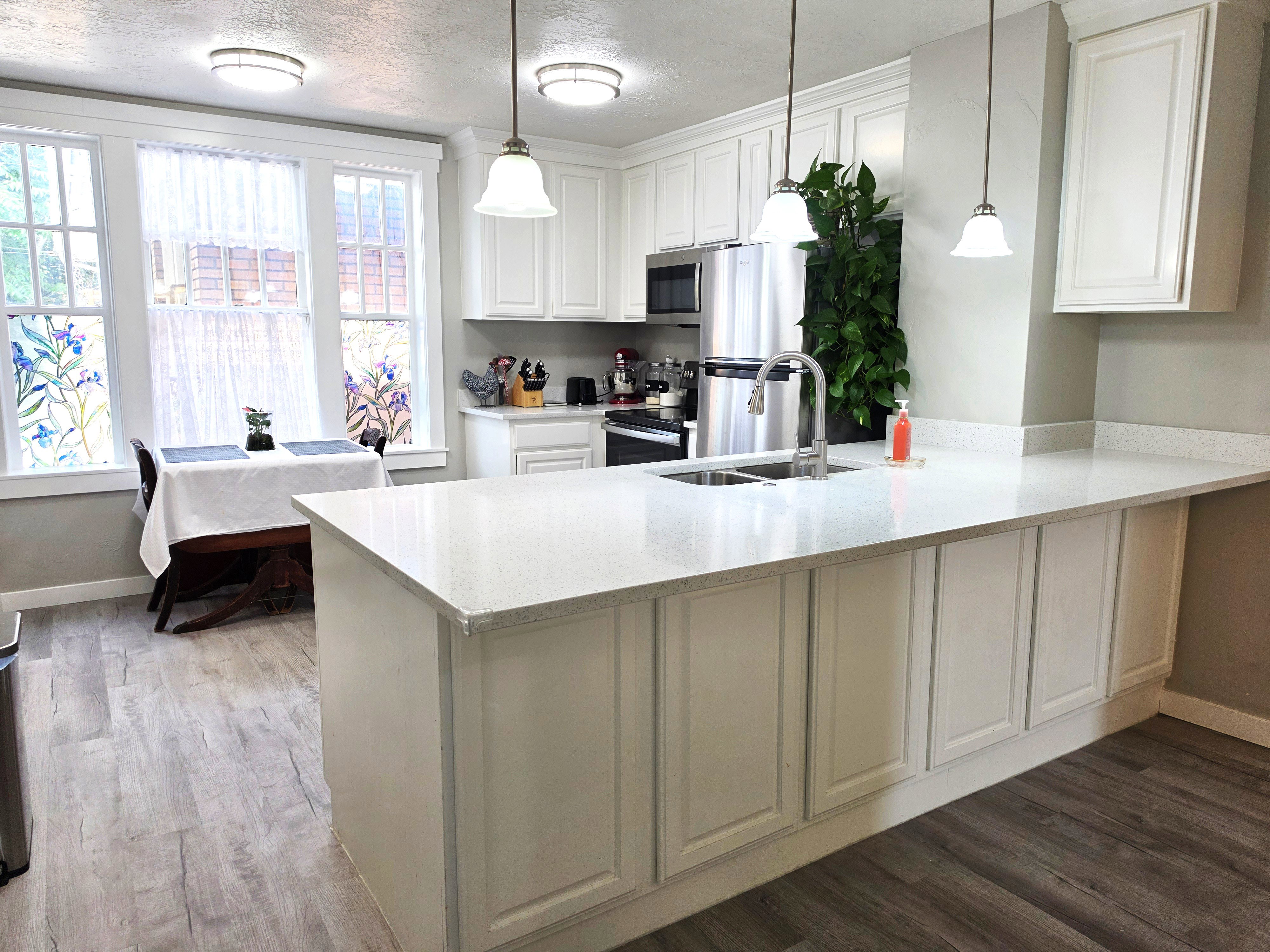 Kitchen with white cabinetry, light-colored countertops, stainless steel appliances, and wood-finish flooring