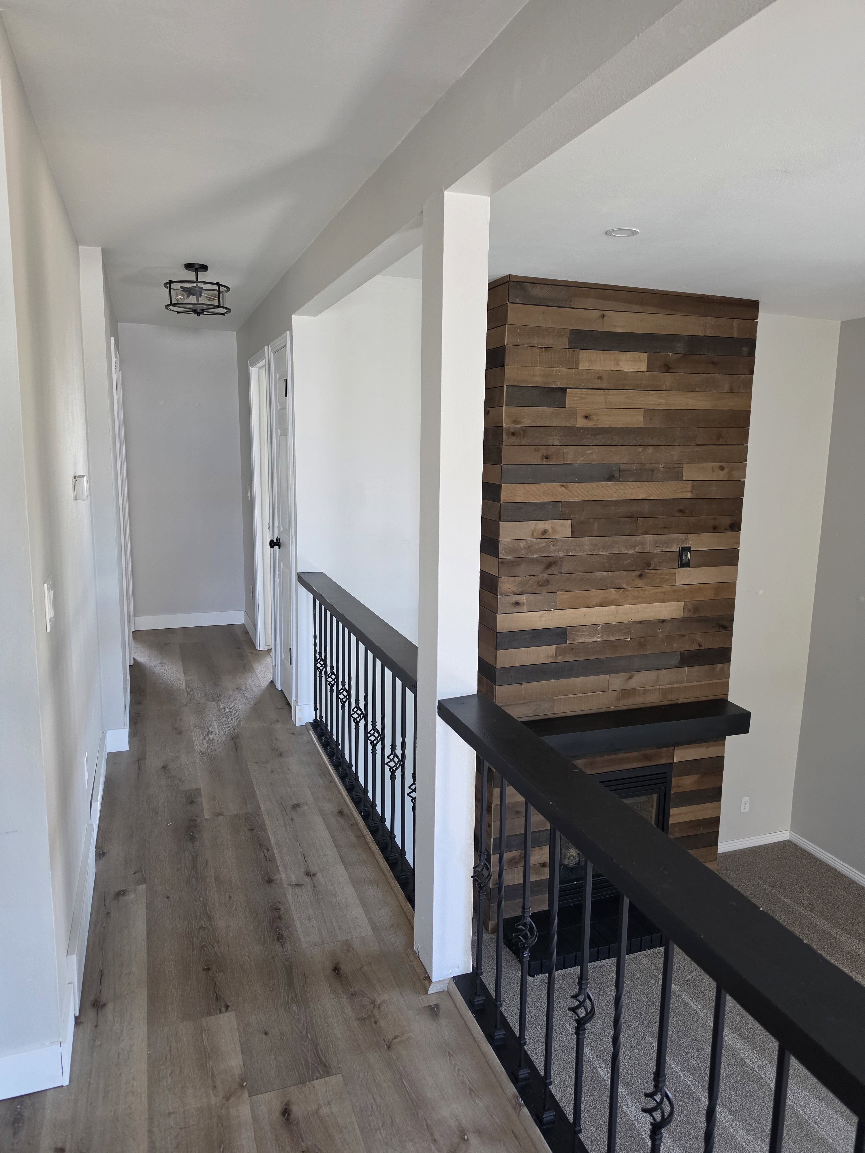 Open concept upper landing featuring wood-finish flooring, a decorative black metal railing, and a modern ceiling light fixture