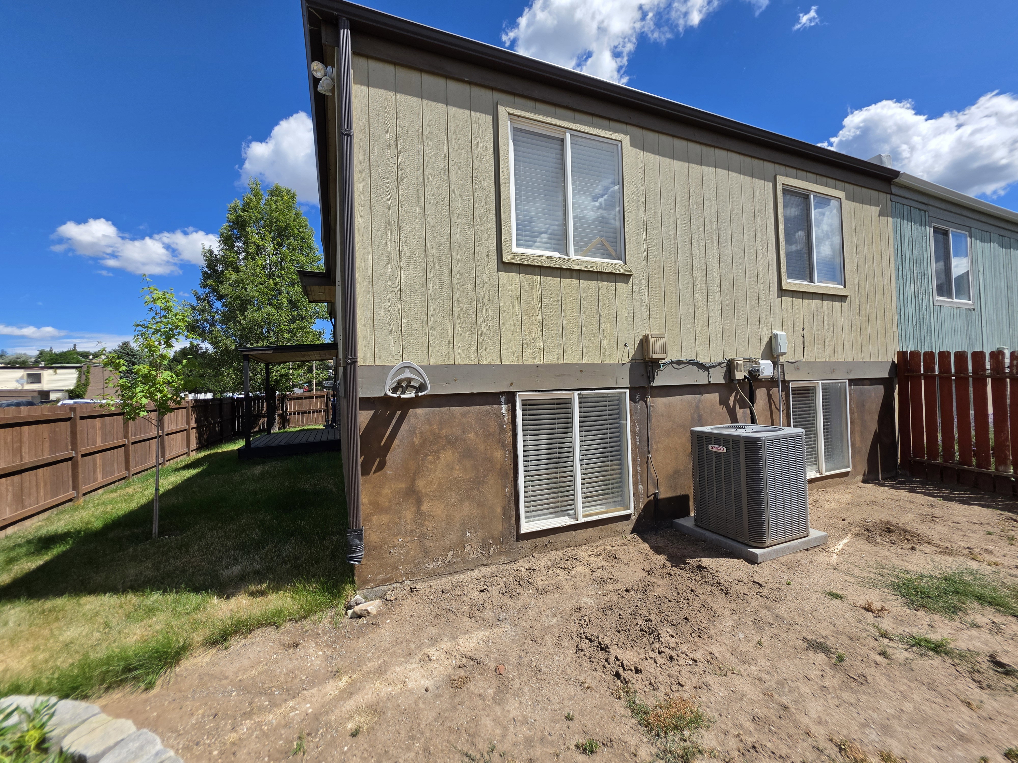 Exterior property view featuring light-colored siding, a brown privacy fence, and a grass area with a young tree