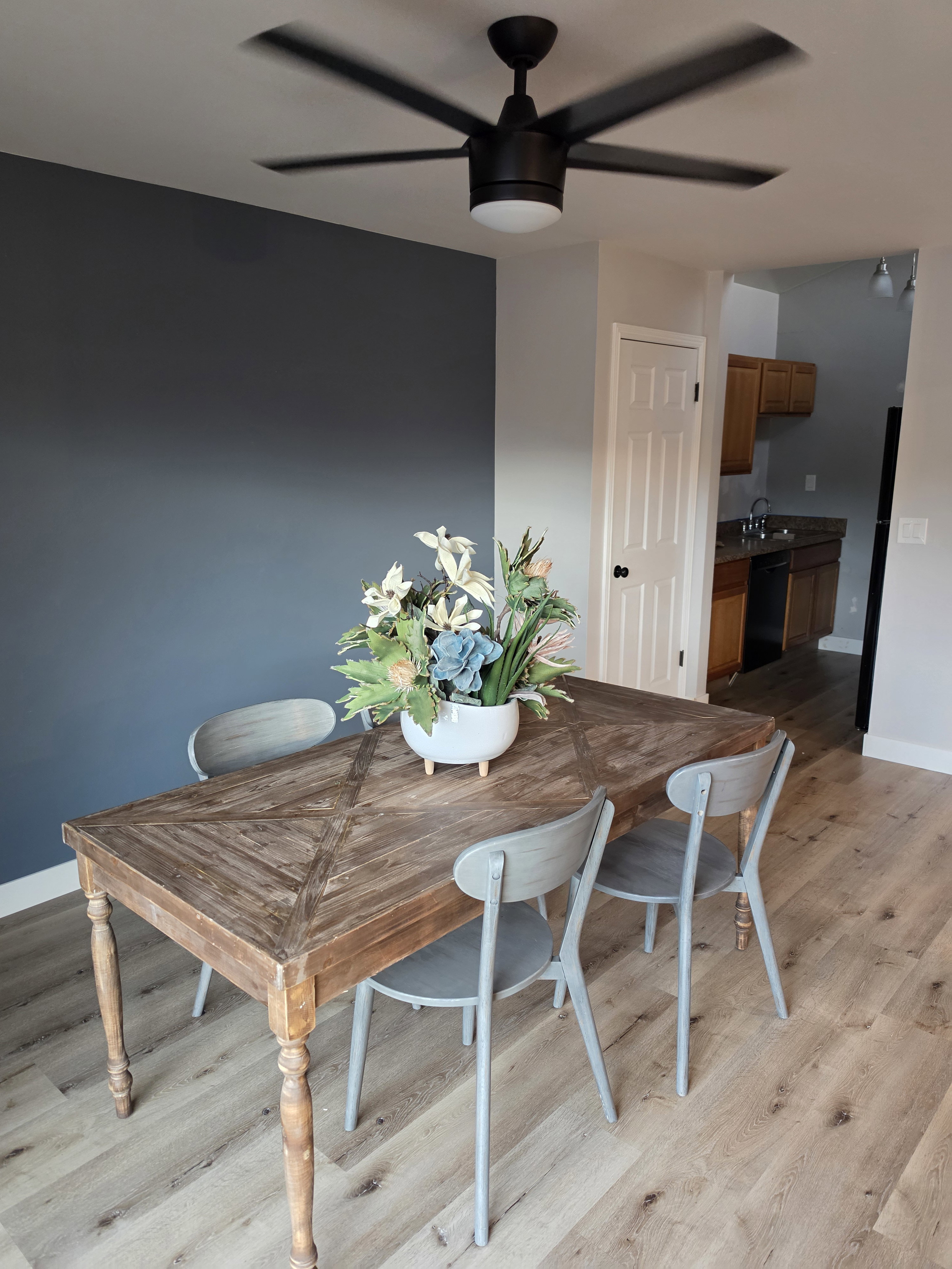 Dining area featuring a modern black ceiling fan with integrated lighting, a striking accent wall, and wood-finish flooring