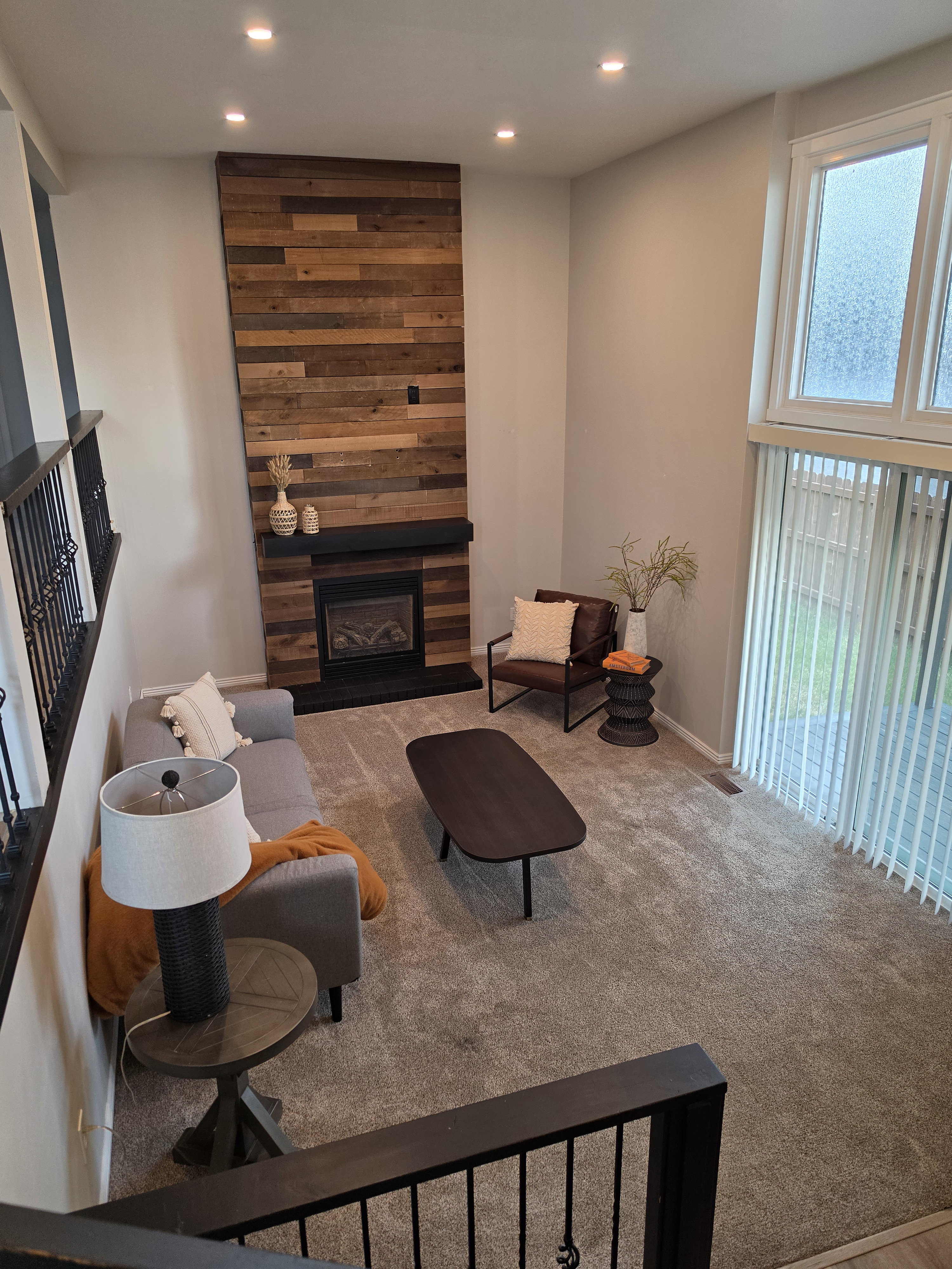 Living area featuring a floor-to-ceiling accent wall with wood paneling and a fireplace with a black mantel