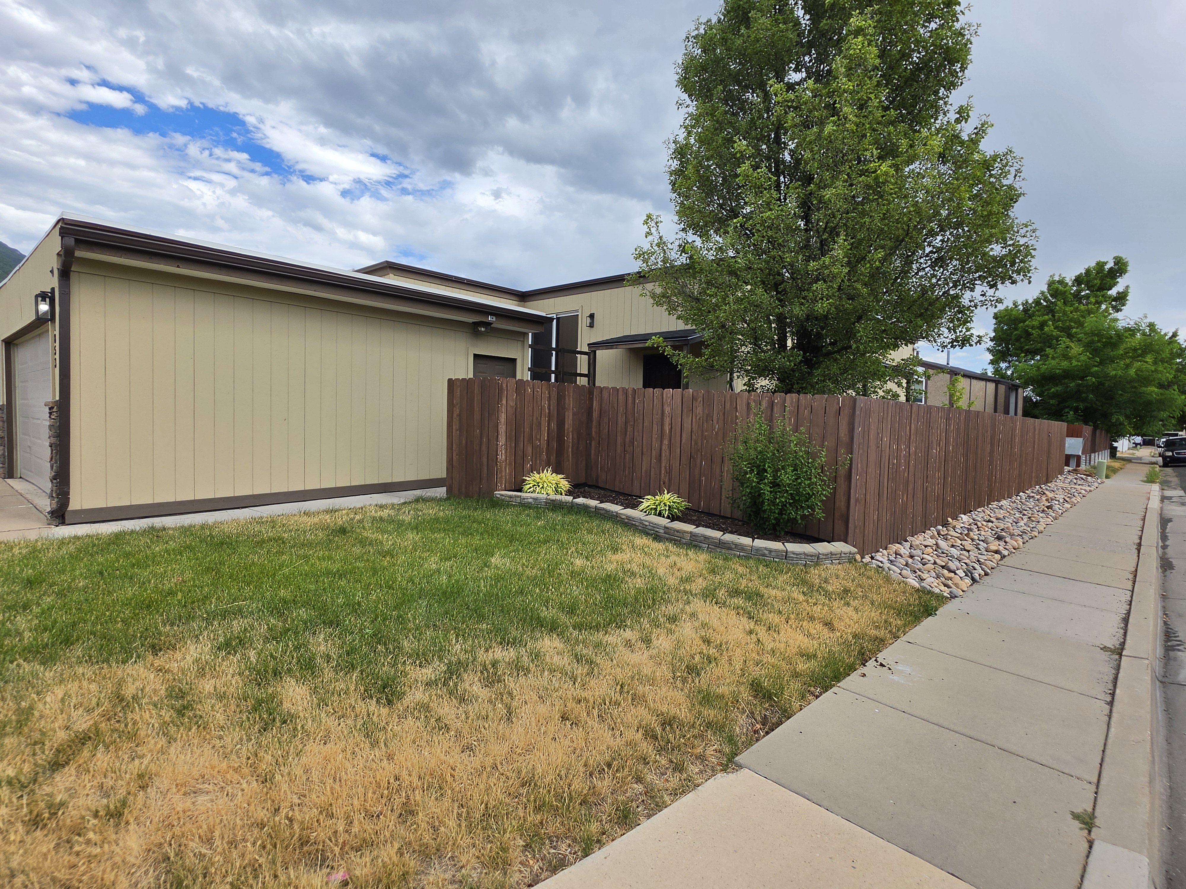 Exterior featuring tan siding, a brown privacy fence, and a two-car garage with stone veneer accents