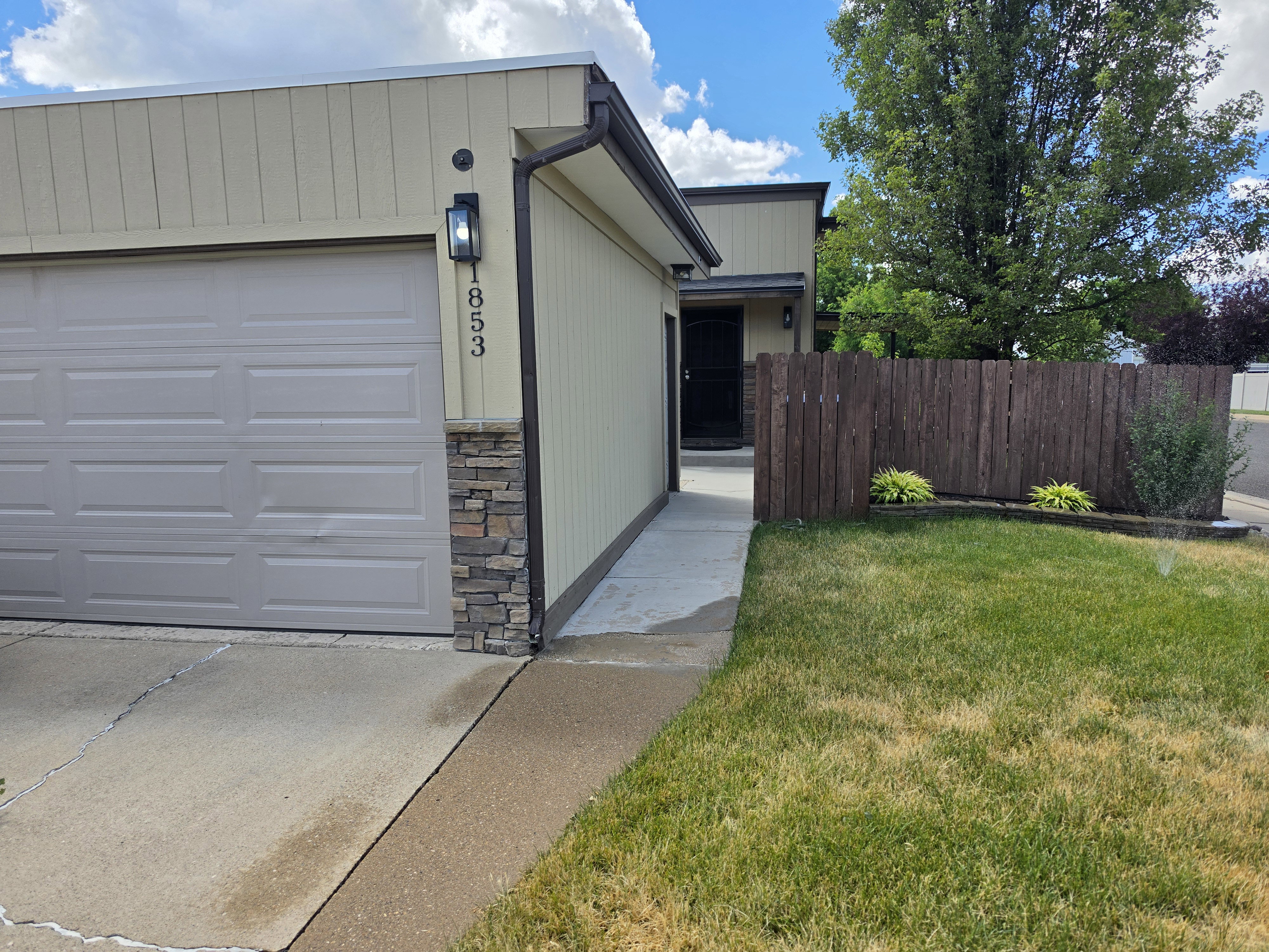 Exterior featuring a light tan facade, attached garage, stone accents, and a dark brown privacy fence