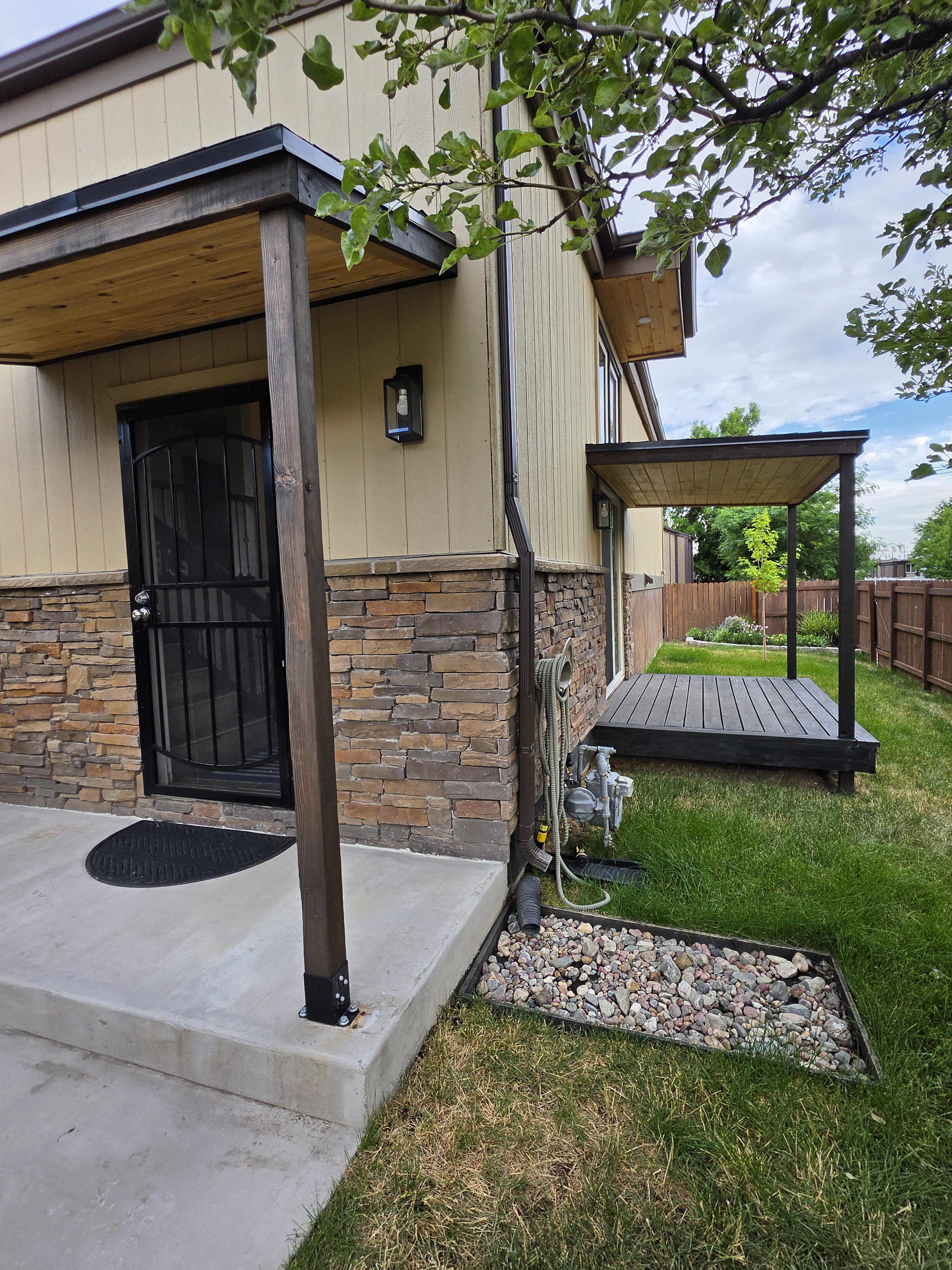 Exterior featuring stacked stone accents, vertical siding, a covered entry with wood-finish ceiling, and a covered patio with dark wood-finish decking