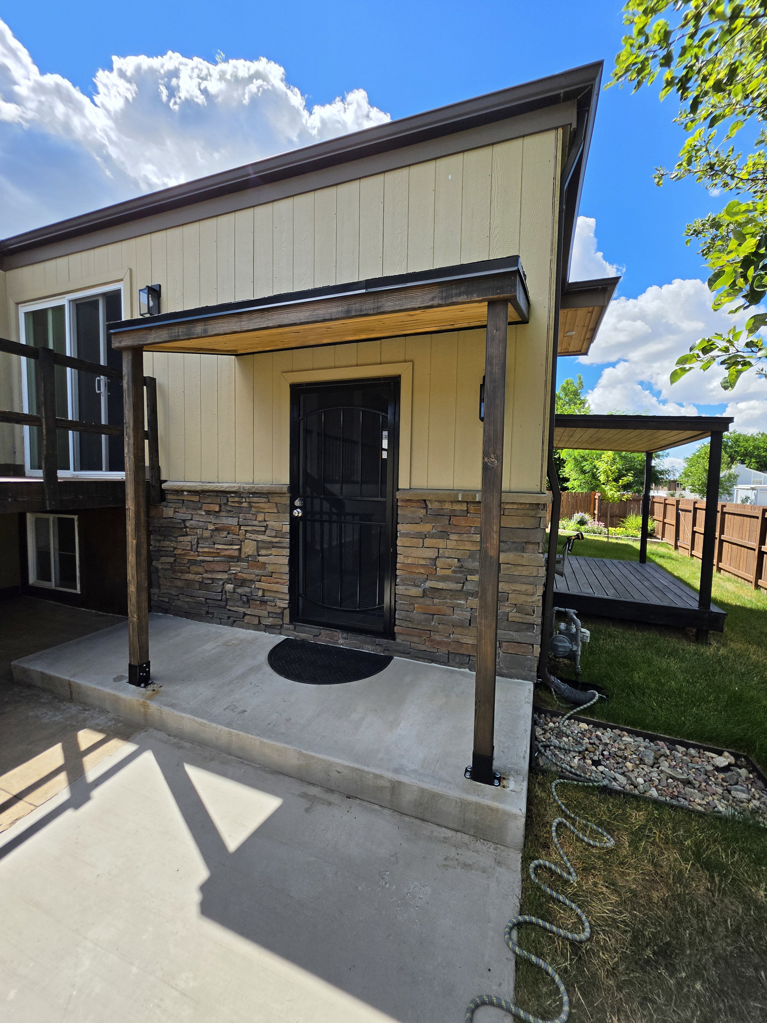 Contemporary exterior featuring horizontal siding, a stone veneer accent, and a covered entry with exposed wood beams