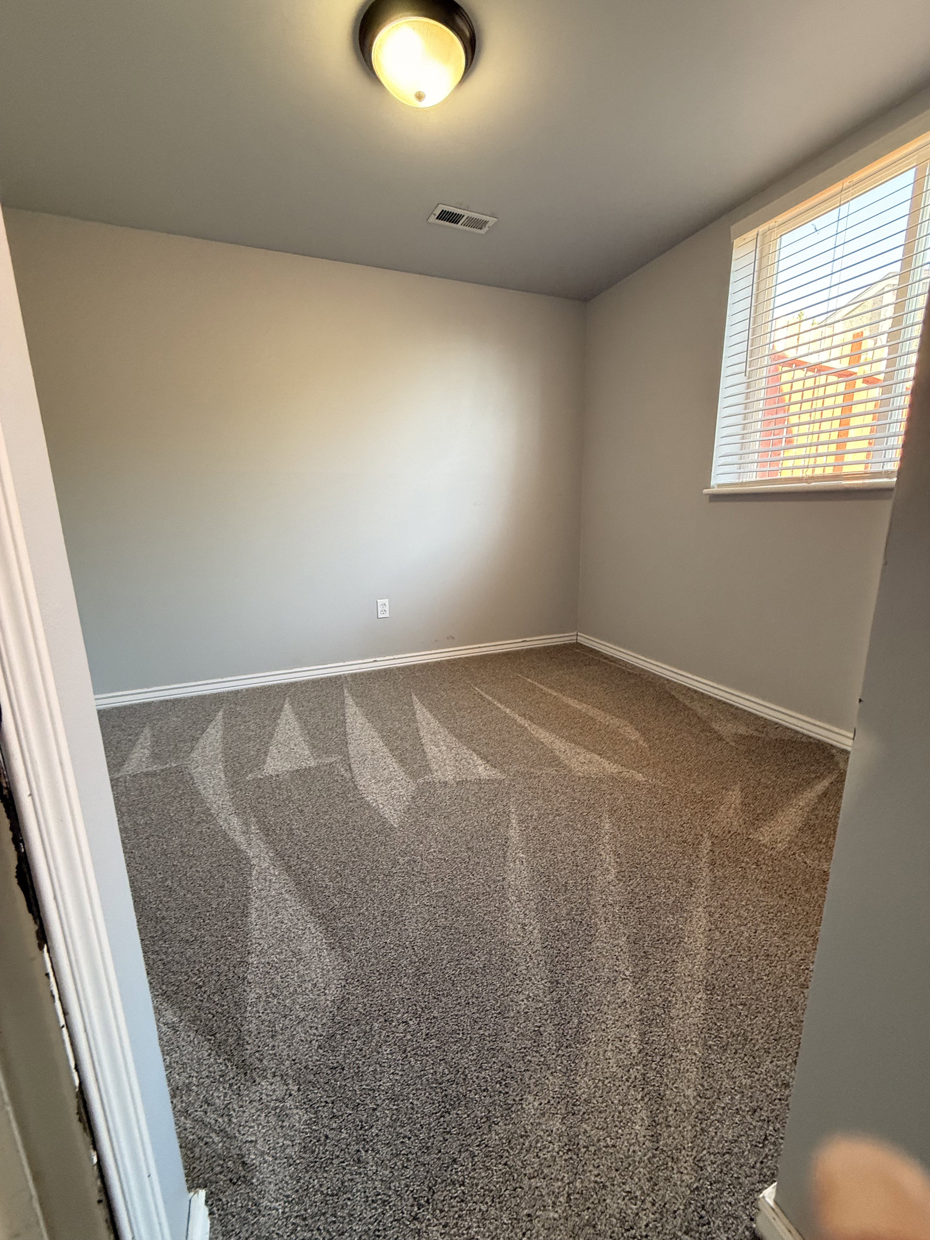 Interior room featuring light gray wall paint, white baseboards, and a neutral-toned carpet with visible vacuum lines