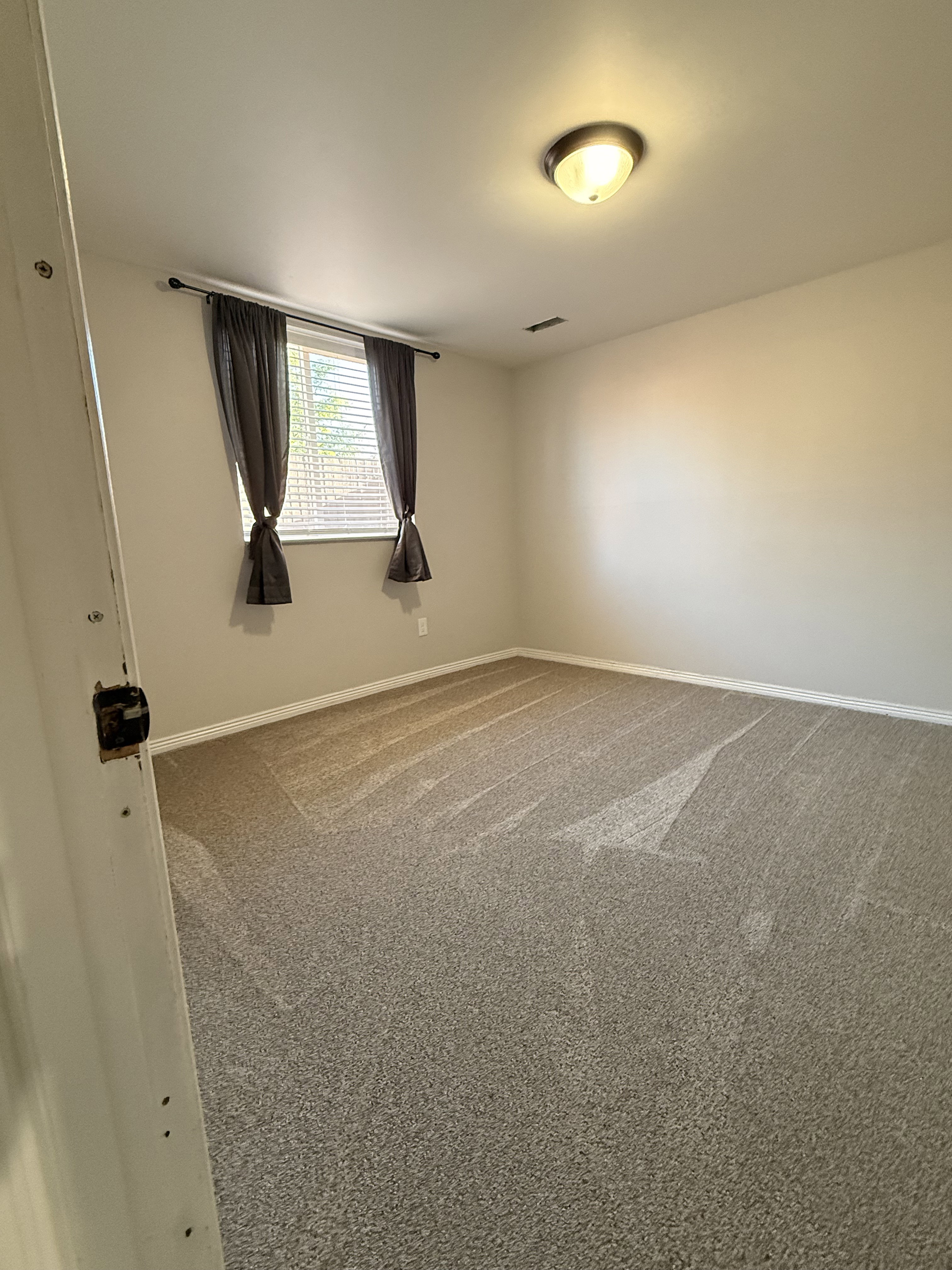 Carpeted room featuring a single window with blinds, ceiling-mounted light fixture, and white baseboards