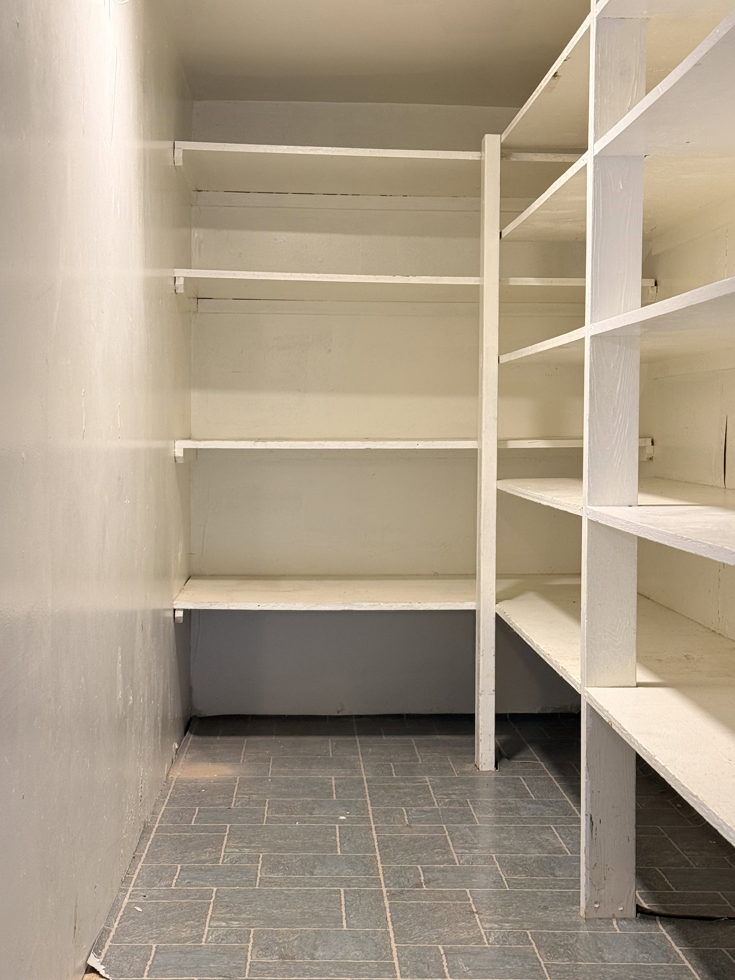 Built-in pantry shelving featuring multiple tiers of storage, painted white finishes, and durable tile flooring
