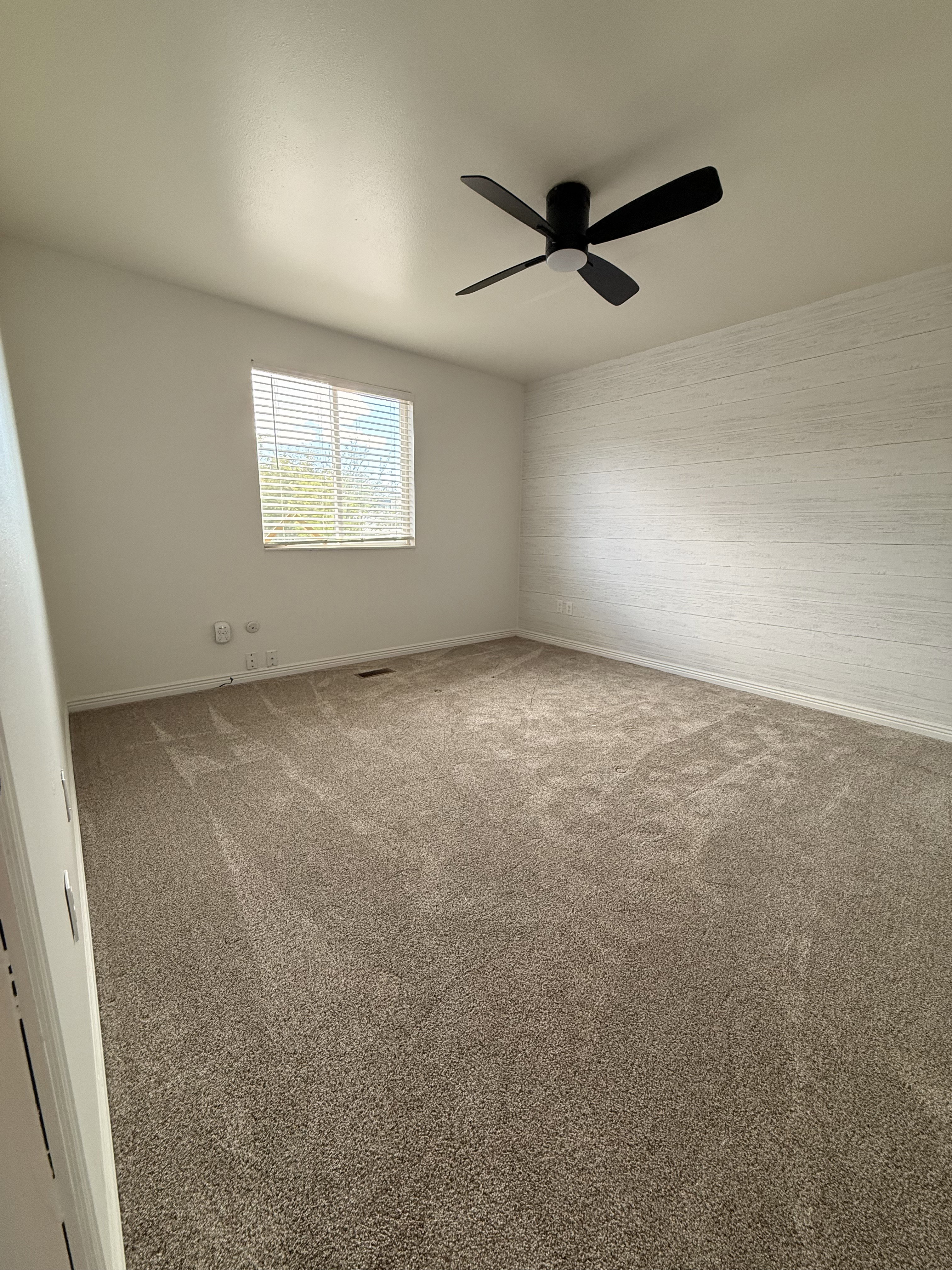 Spacious room featuring neutral carpeting and a window with horizontal blinds