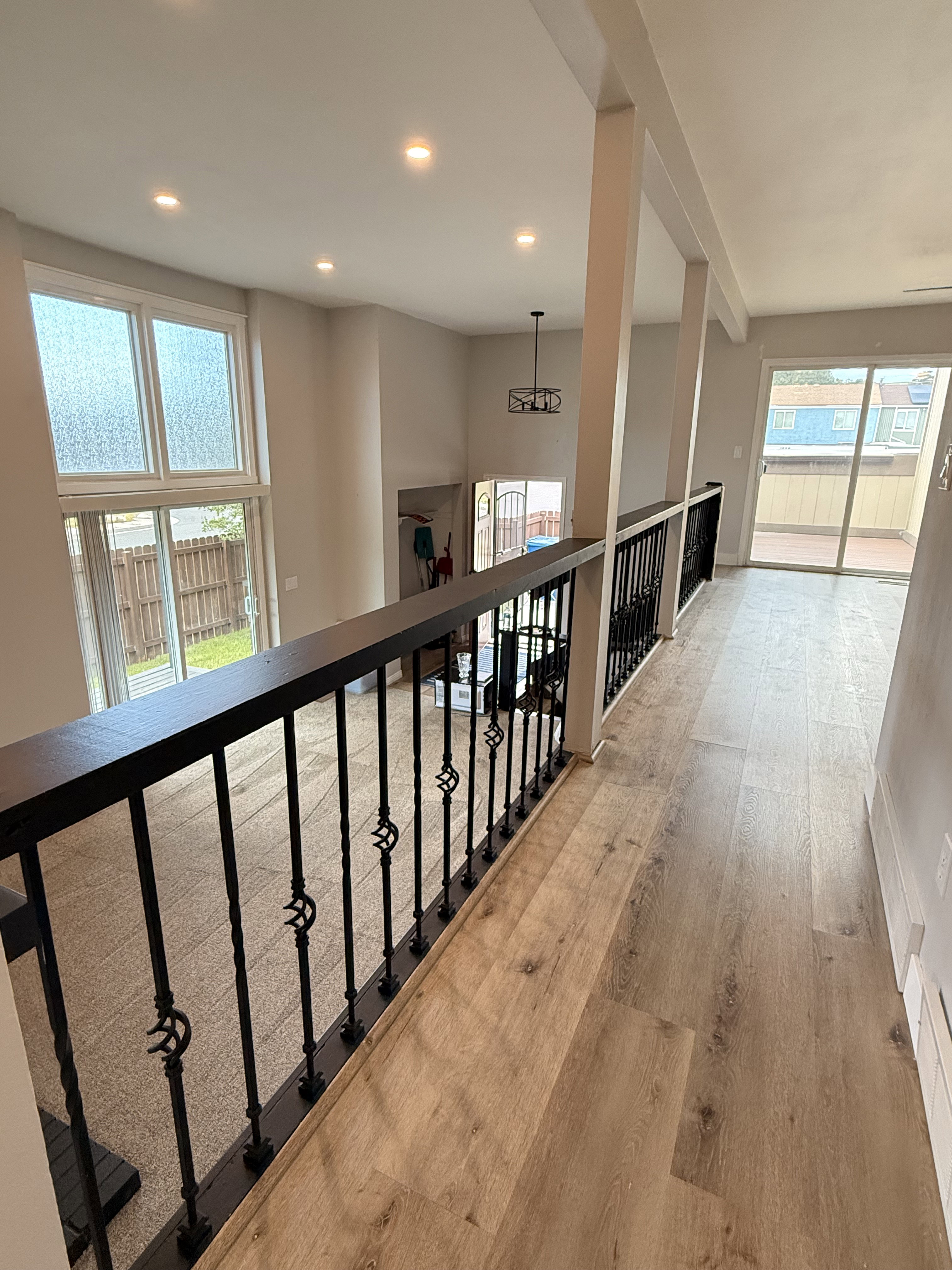 Interior loft area featuring wood-finish flooring, an ornate wrought iron railing, recessed lighting, and a contemporary chandelier