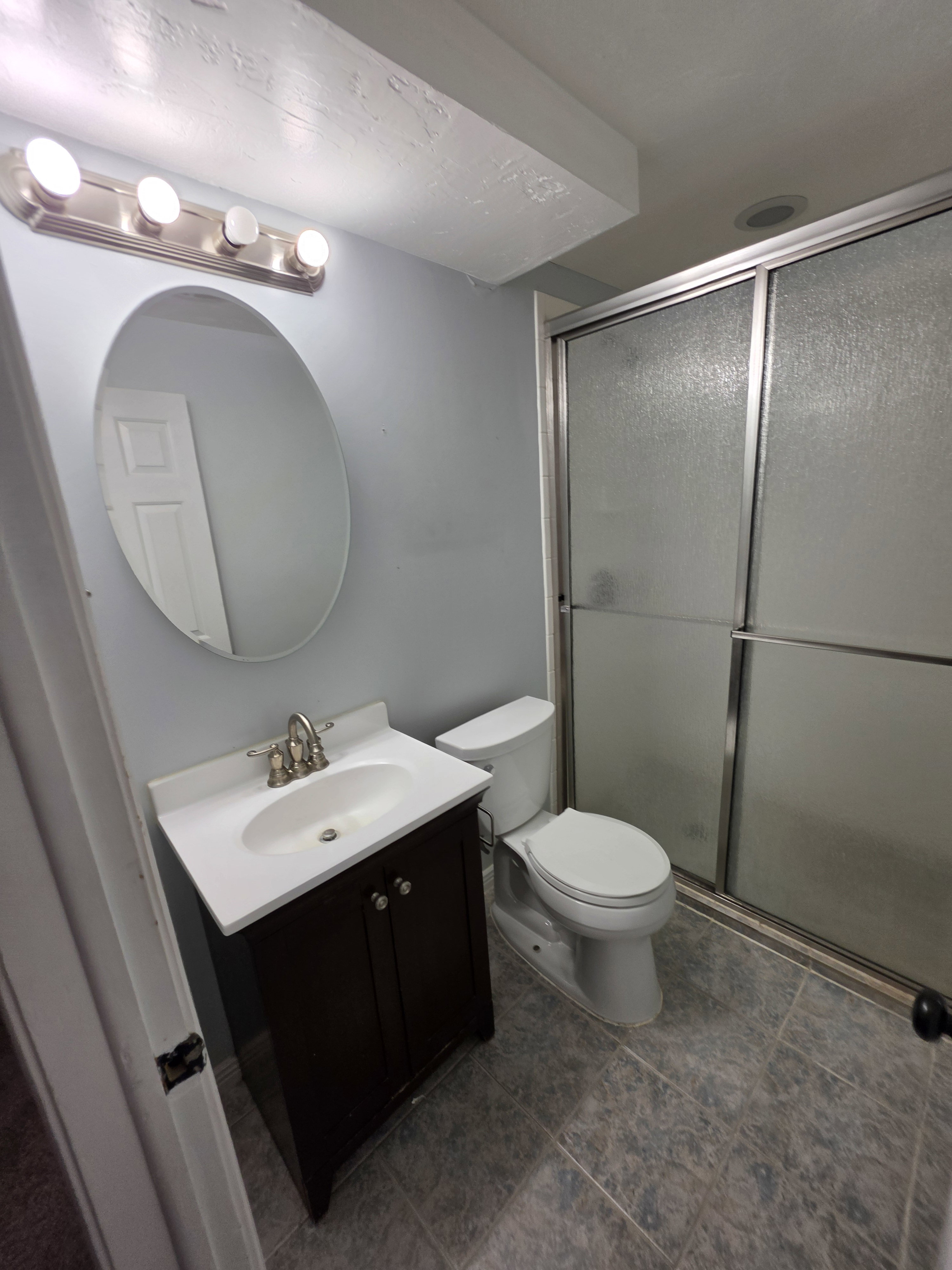 Bathroom featuring a dark wood-finish vanity with a white countertop and oval undermount sink, a chrome vanity light fixture, and a sliding glass shower enclosure