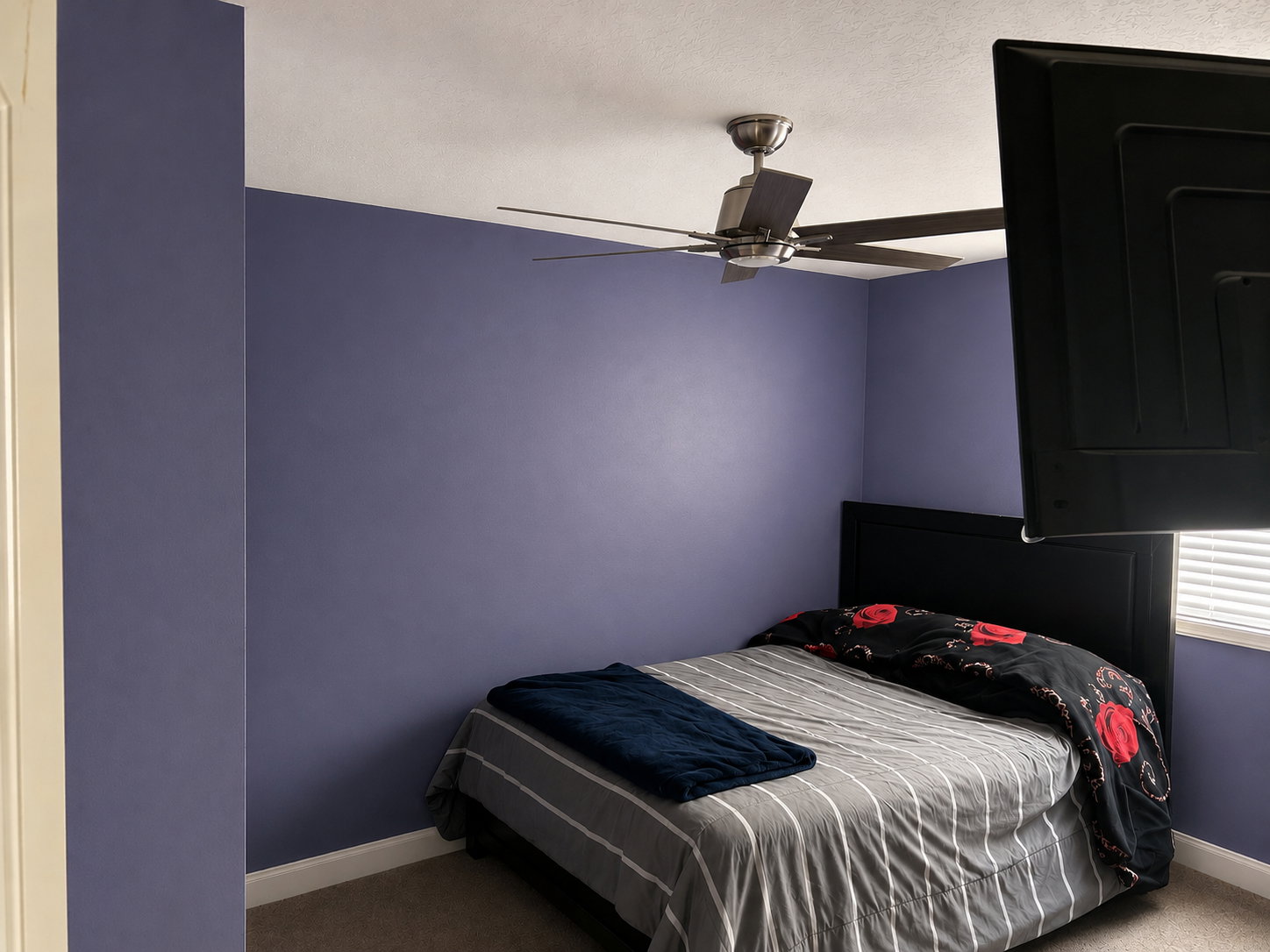 Bedroom featuring a dark-toned ceiling fan, light-toned window blinds, and a built-in wall-mounted television bracket