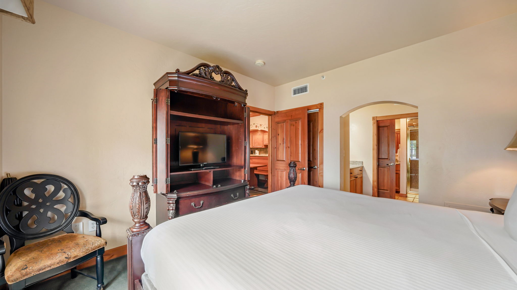 Primary bedroom featuring light-toned walls, wood-finish flooring, an entertainment armoire, a decorative archway to bathroom, and wood panel doors