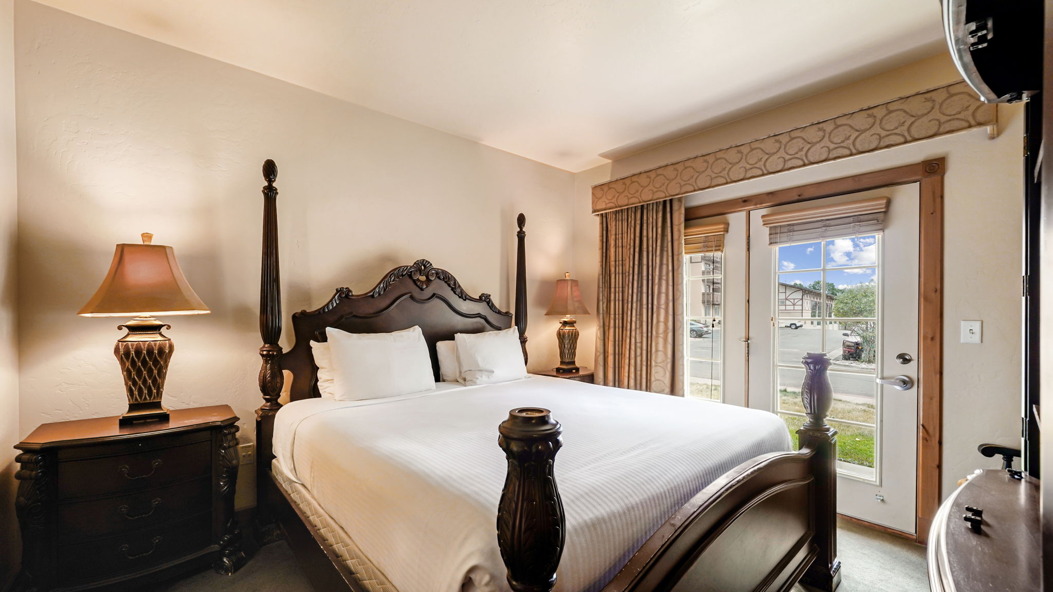 Primary bedroom with main level french doors to small private patio, carved wood-finish bed frame, nightstand, and dresser