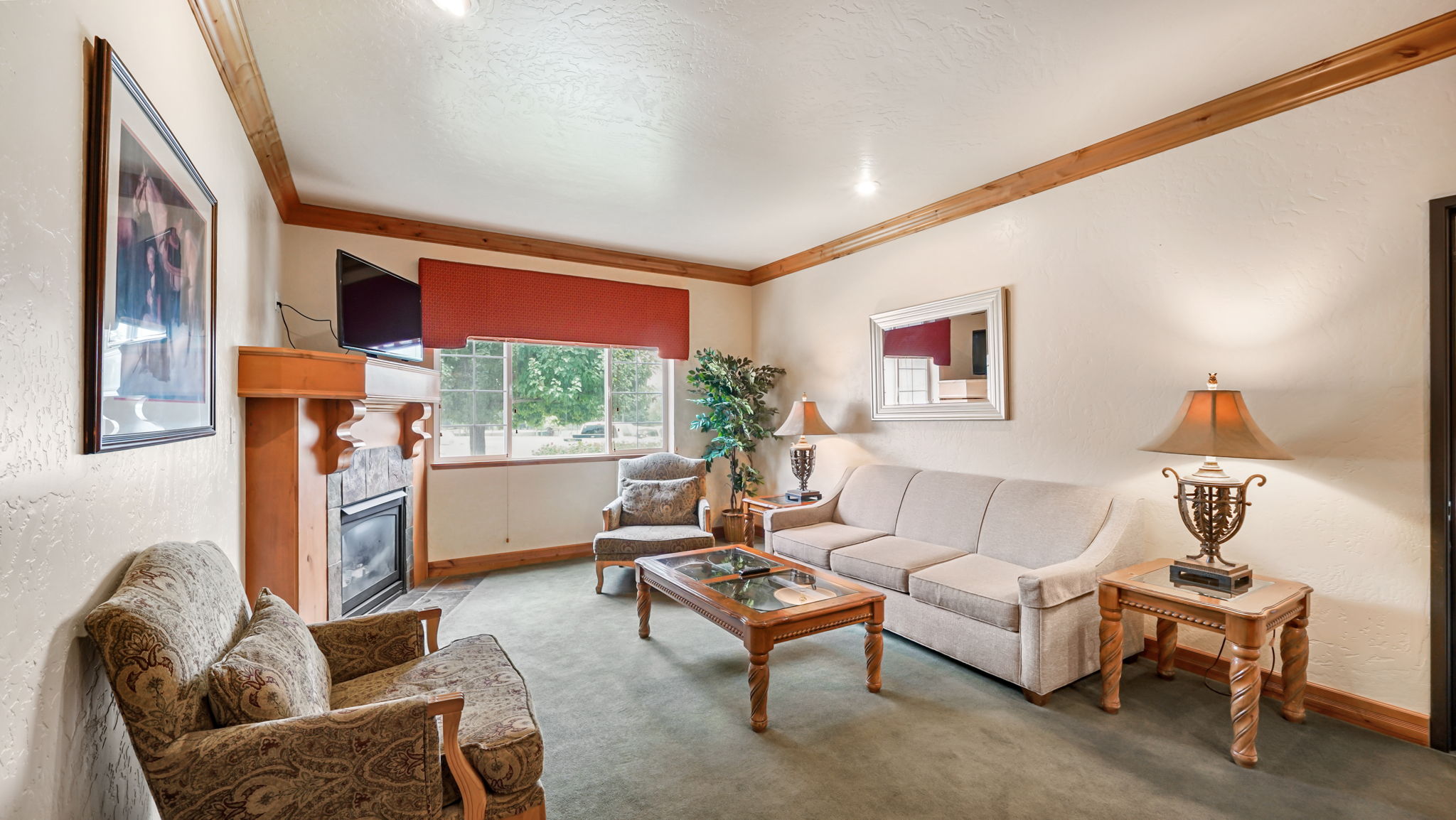 Living area featuring a fireplace with a stone surround and wood mantel, large window with a red valance, wood-finish ceiling trim, and recessed lighting