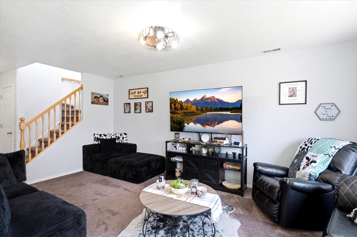Living area featuring neutral wall tones, carpet flooring, a natural wood staircase with balusters, a built-in entertainment console, and a contemporary ceiling light fixture