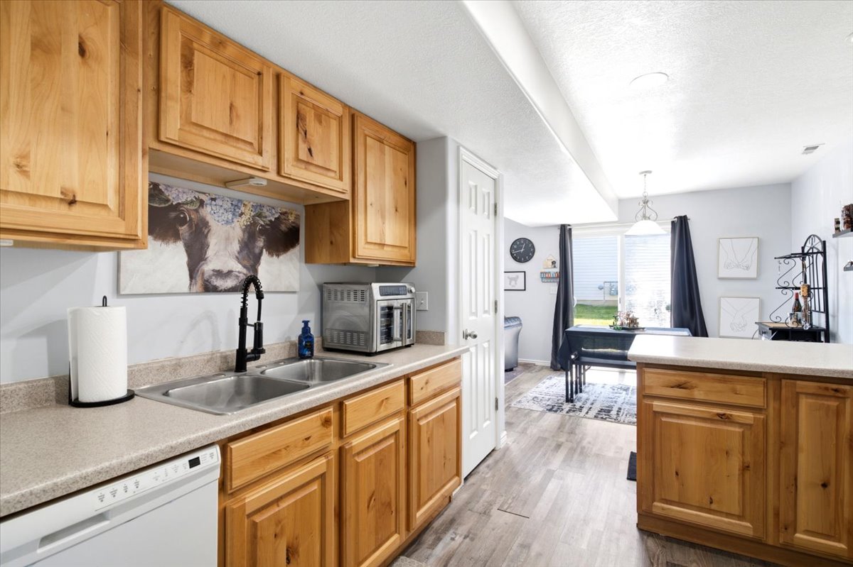 Kitchen featuring natural wood-finish cabinetry, a dual-basin stainless steel sink with a matte black faucet, laminate countertops, and a built-in dishwasher