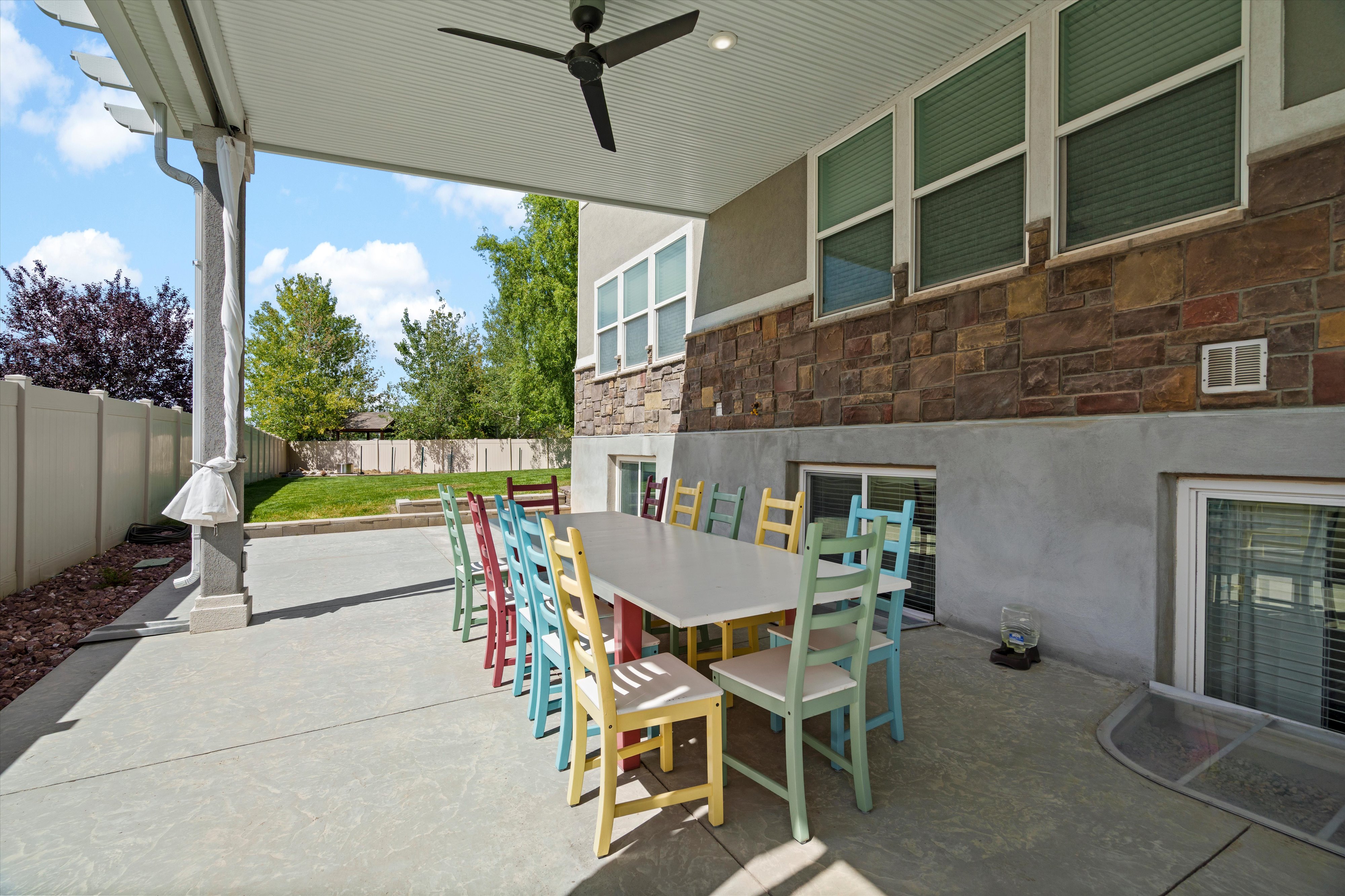 Covered patio featuring a ceiling fan, concrete flooring, and a stone-clad exterior wall