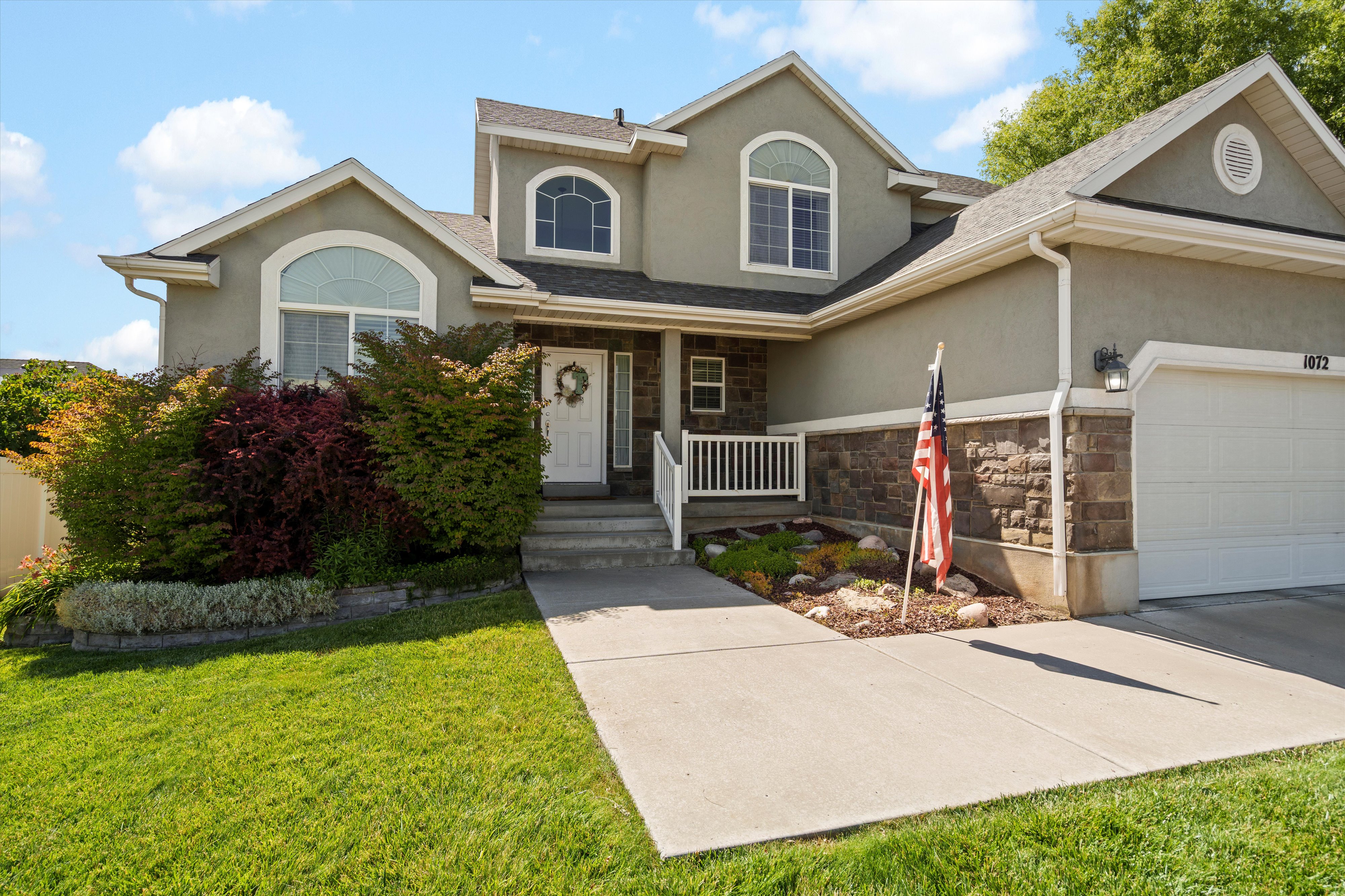 Two-story stucco and stone-accented exterior featuring a concrete driveway, attached two-car garage, and a covered entry with white railing