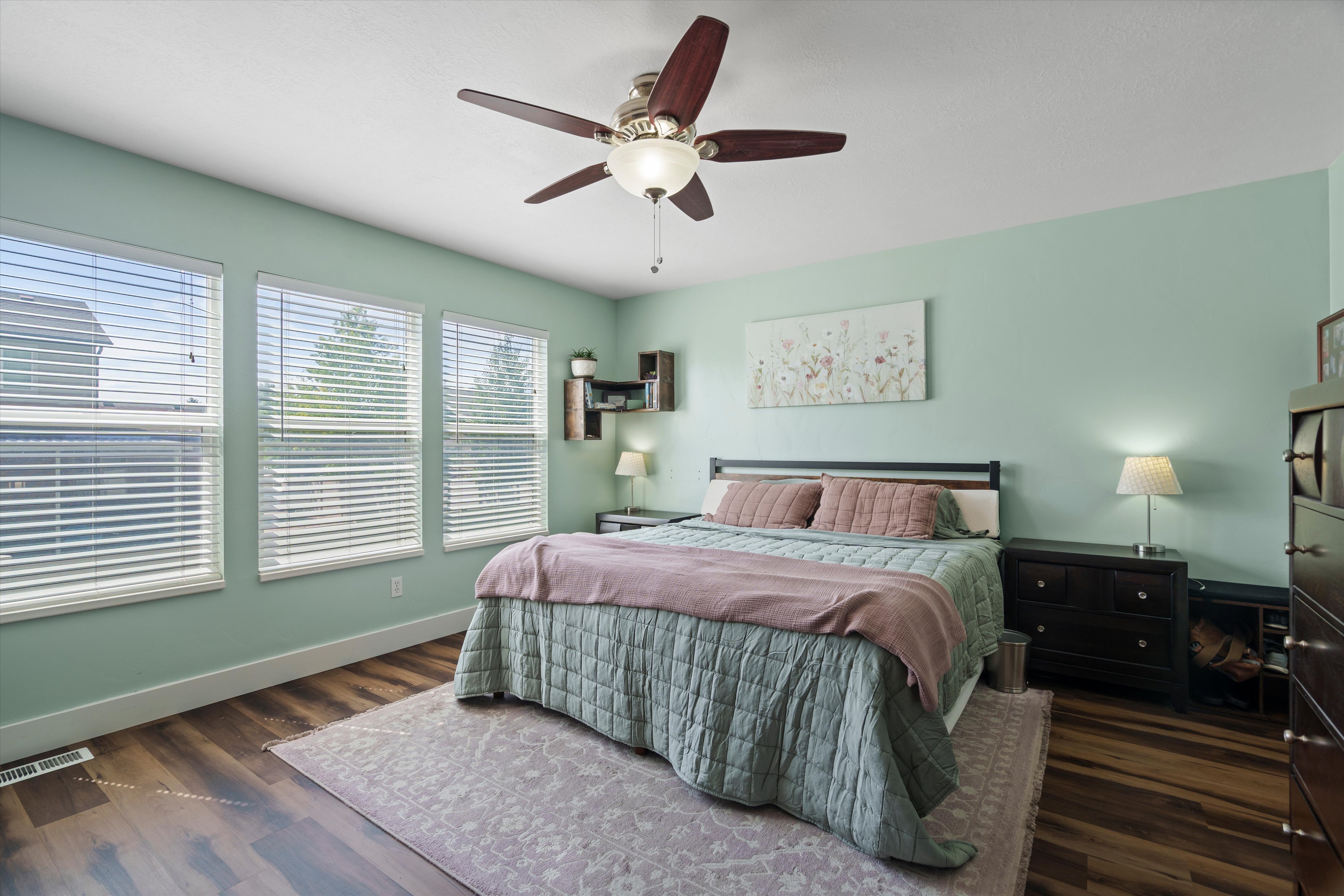 Spacious room featuring wood-finish flooring, three large windows with blinds, and a ceiling fan with integrated lighting