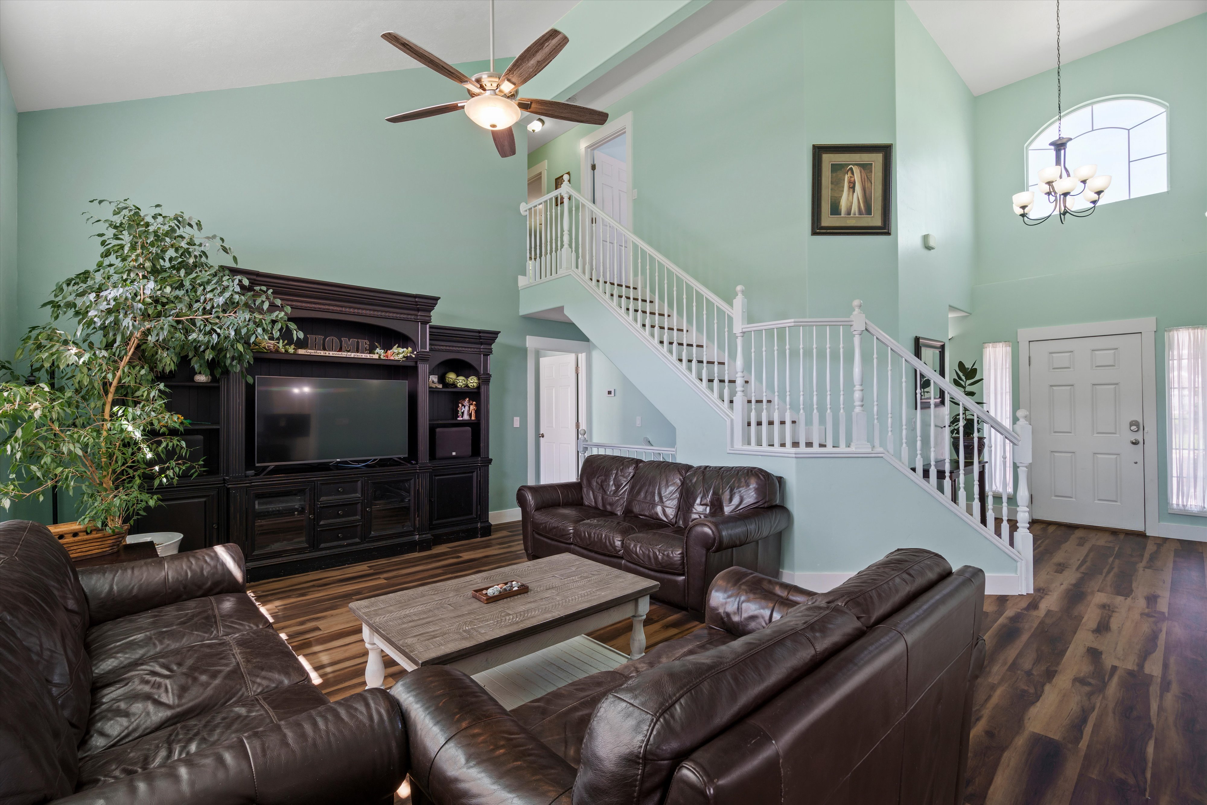 Two-story living area featuring vaulted ceilings, wood-finish flooring, and a prominent staircase with white railings