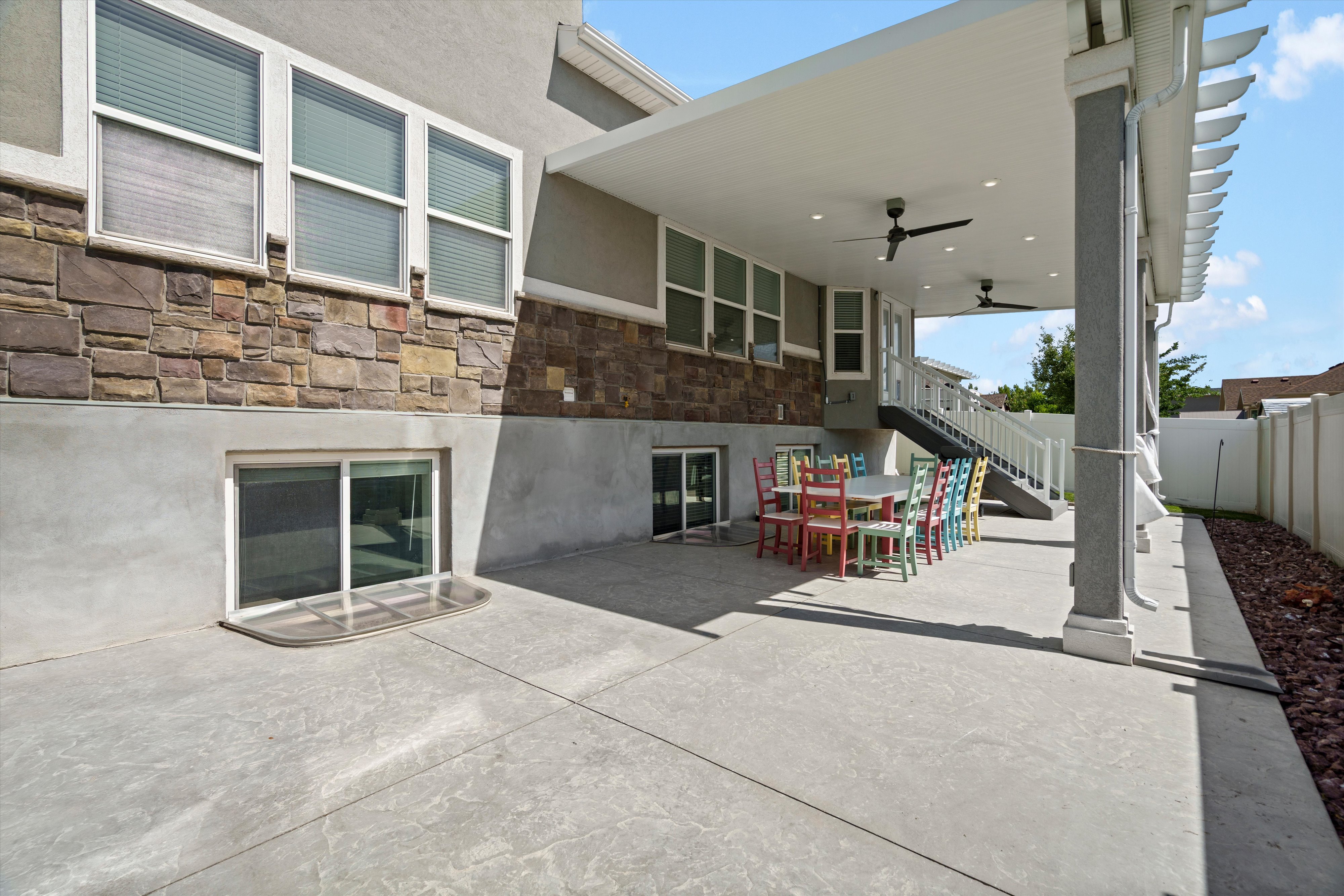 Expansive concrete patio beneath a covered pergola featuring recessed lighting and two ceiling fans