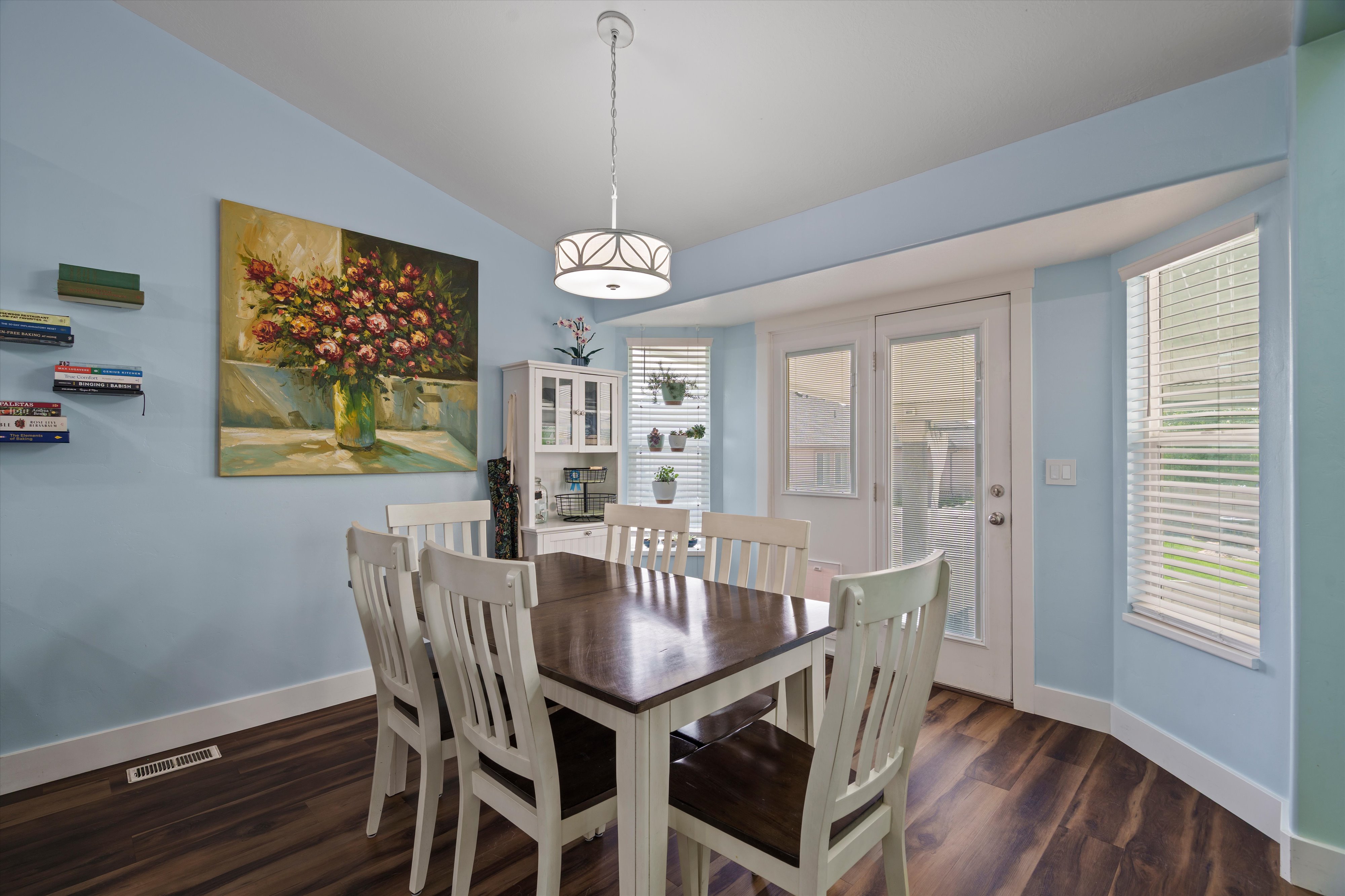 Dining area featuring wood-finish flooring, a contemporary ceiling light fixture, and bay windows with blinds