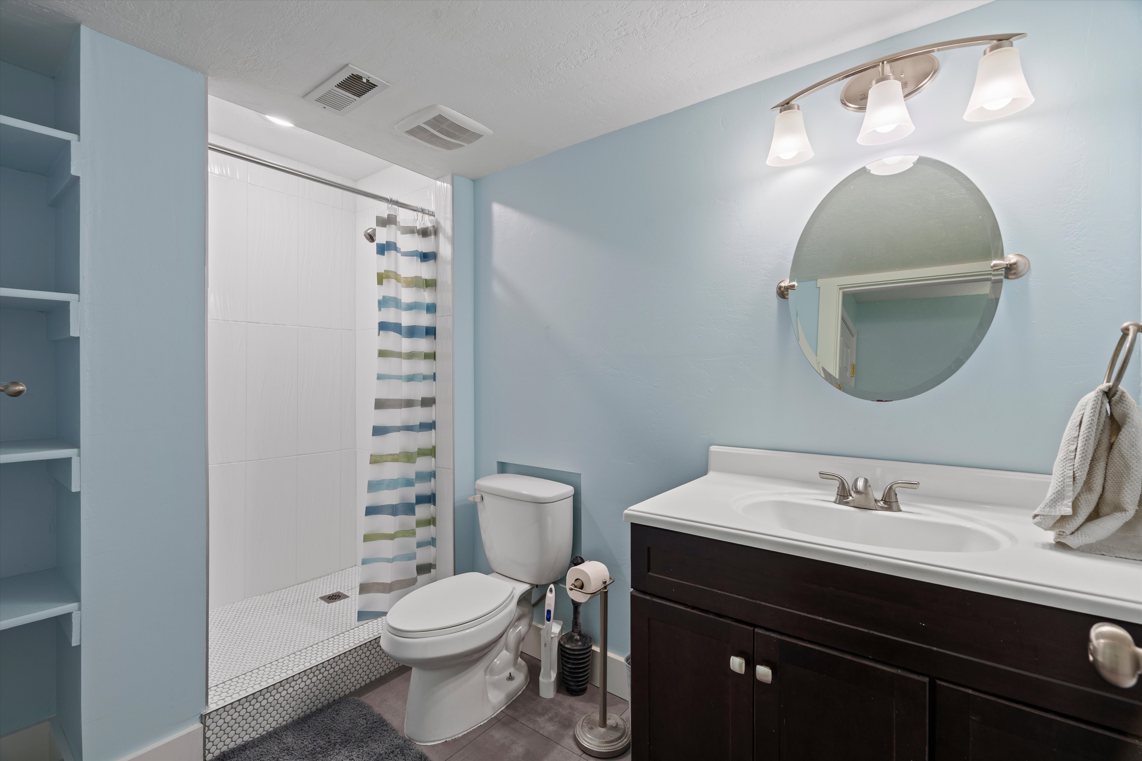 Bathroom featuring a single vanity with dark wood cabinetry, an integrated sink, and a circular mirror